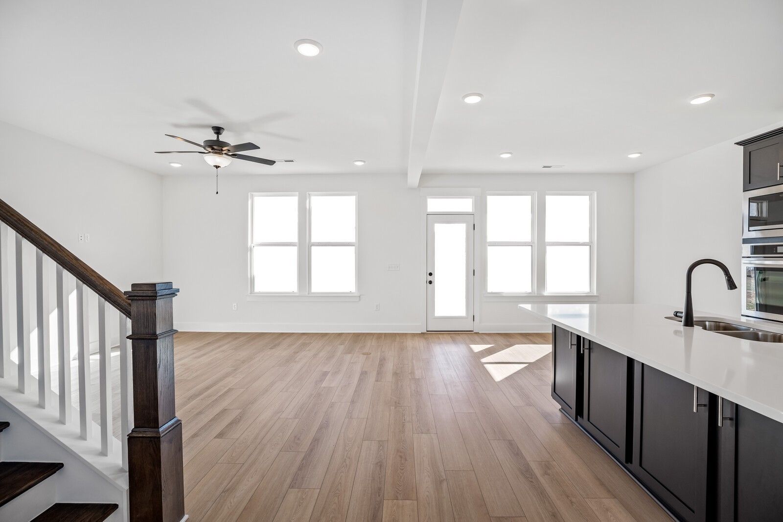 Open-concept kitchen and living space with white quartz island, dark cabinets, stainless appliances, hardwood floors, and staircase in Davidson Homes The Willow C, Gallatin, TN