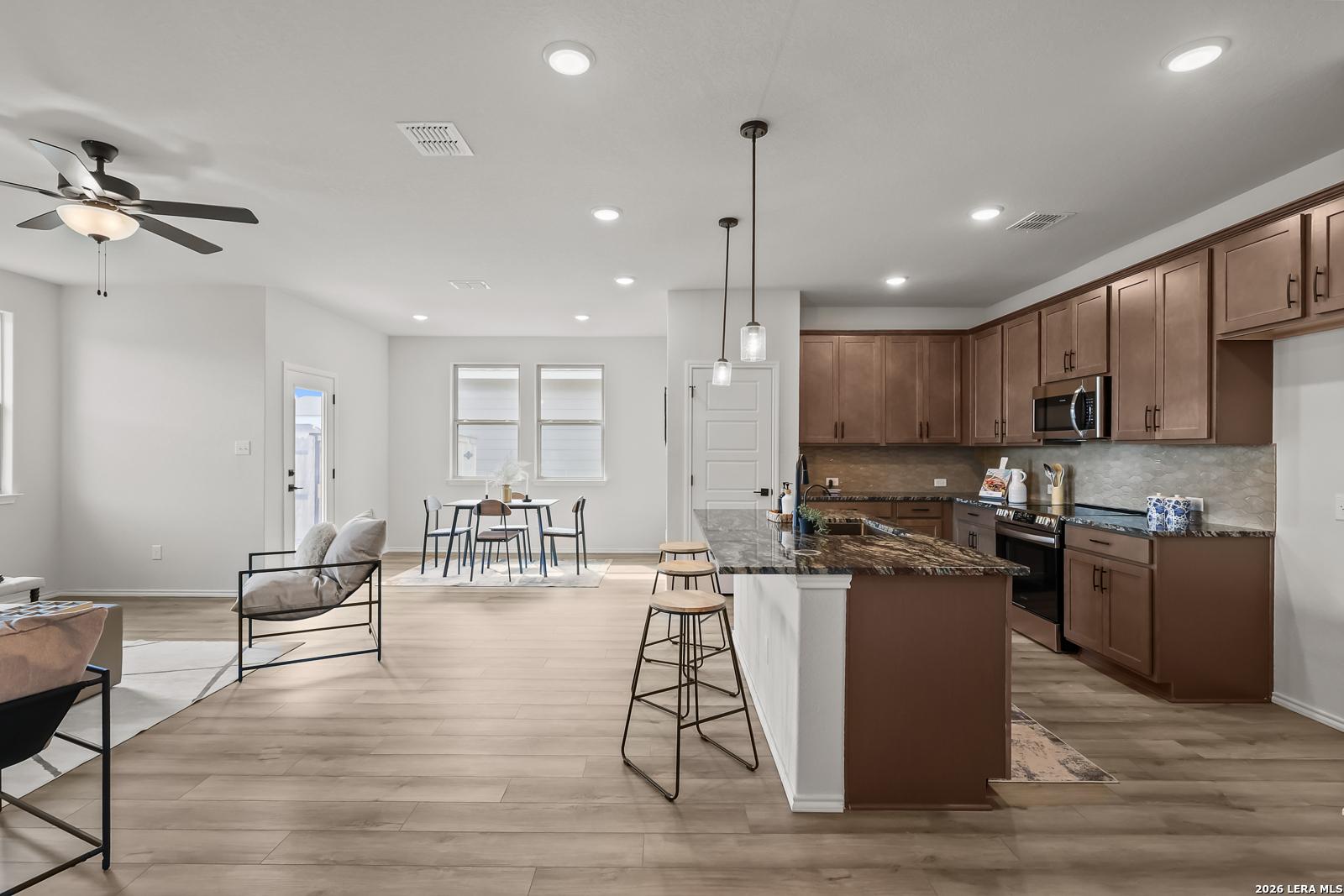 Open-concept kitchen with shaker cabinets, granite island, stainless appliances, and adjacent dining in The Daphne H, Seguin, Texas