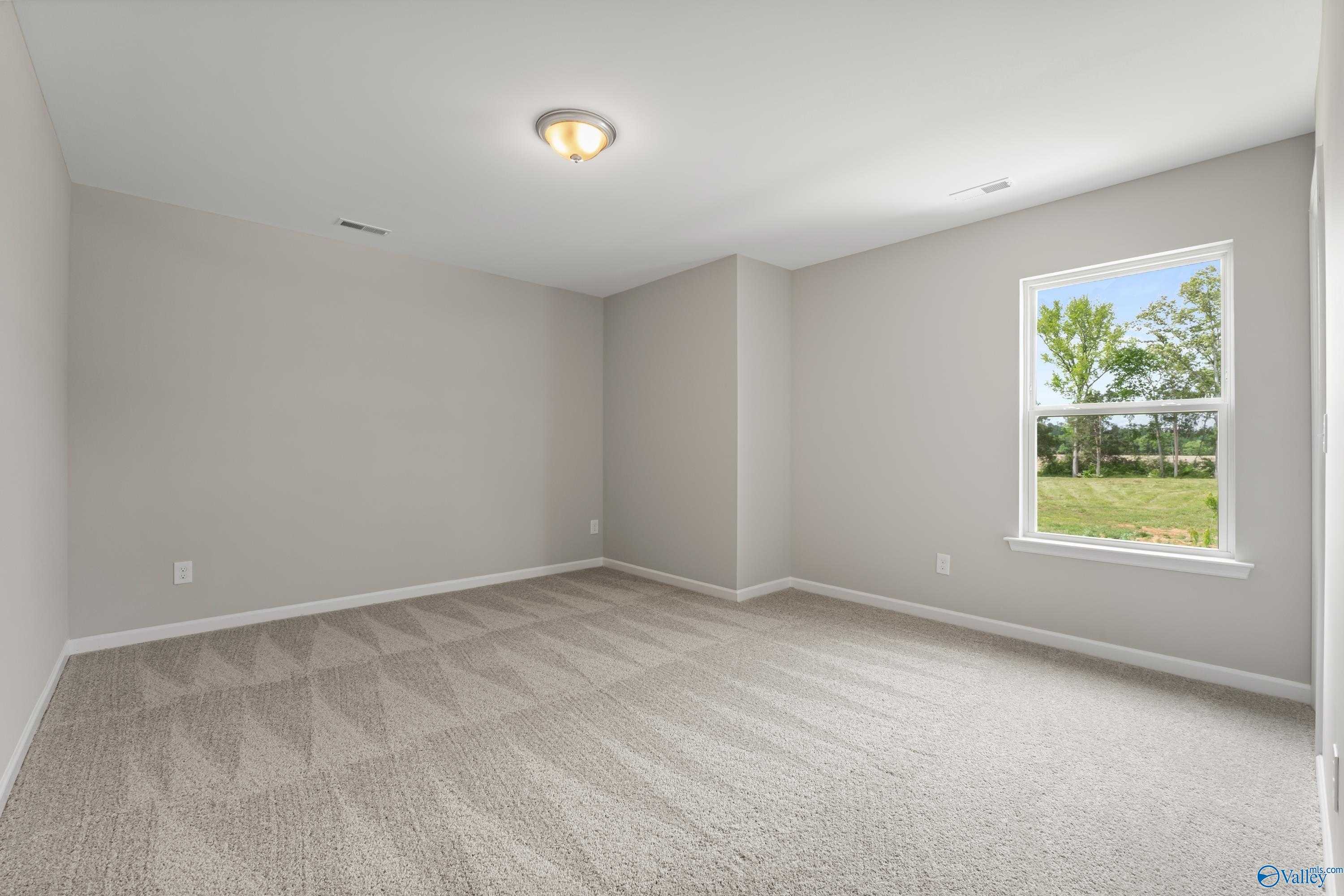 Bright empty bedroom with neutral gray walls, patterned carpet, and window view of green yard in Davidson Homes The Haven, Huntsville