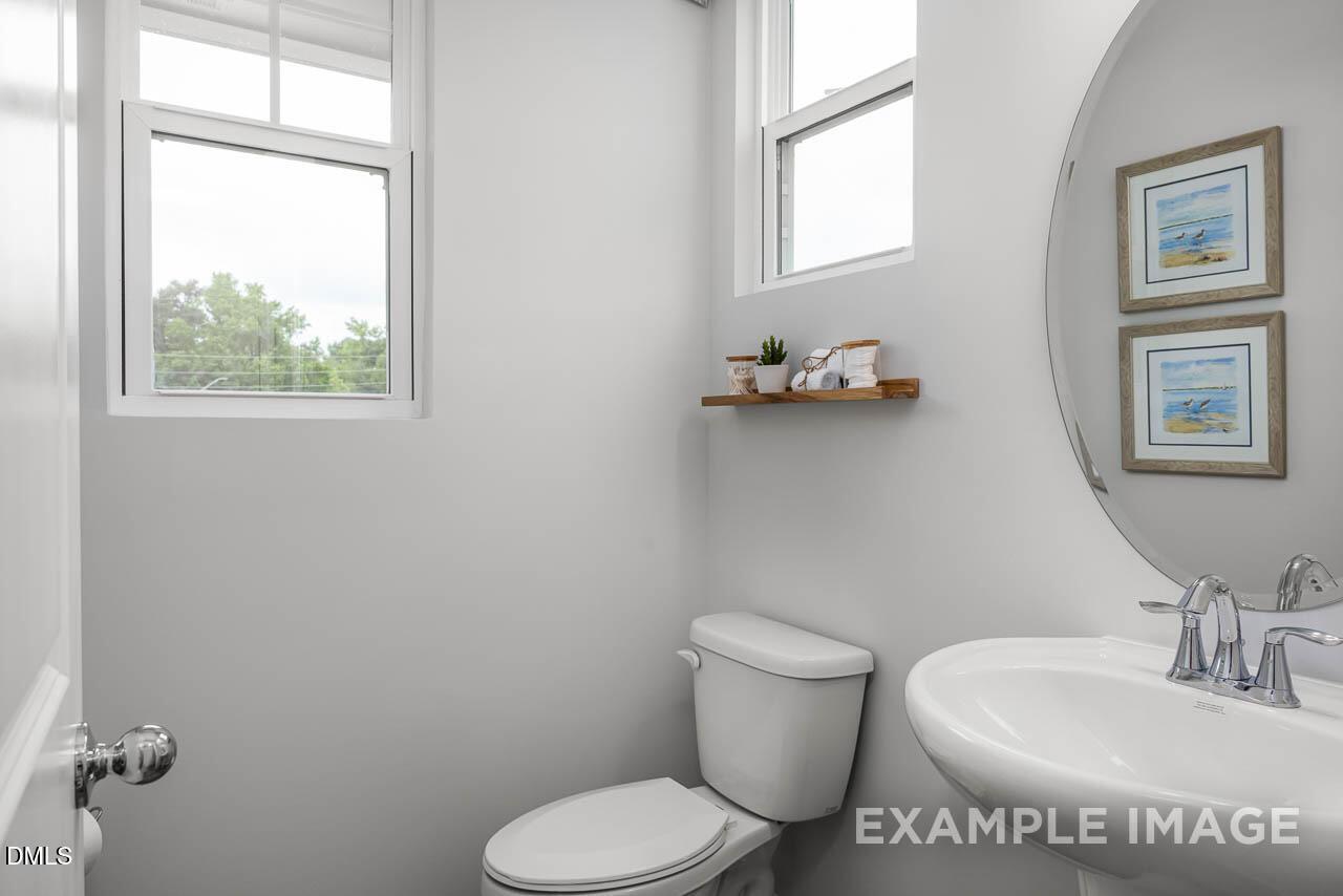 Bright powder room with white pedestal sink, round mirror, beach art, and window in Davidson Homes The Graham, Fuquay-Varina, NC
