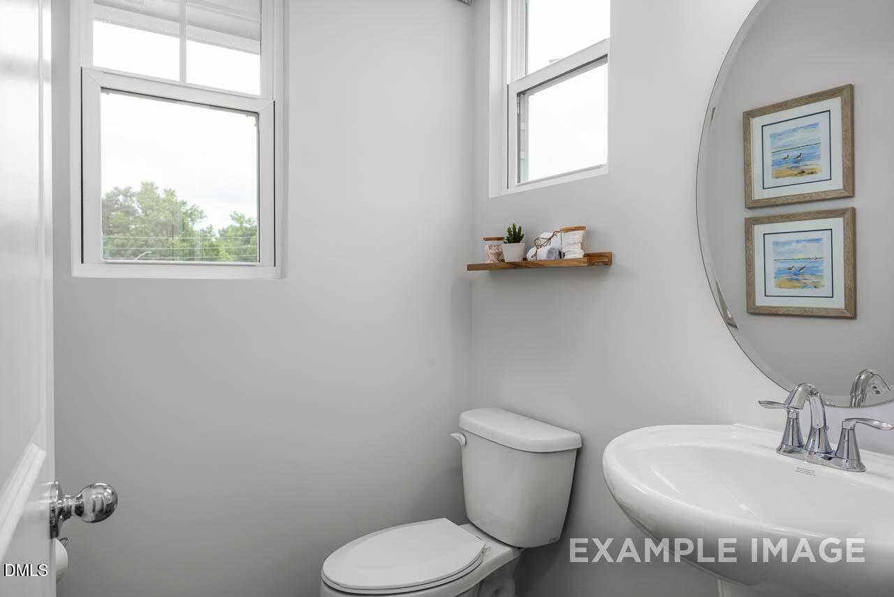 Bright powder room with round mirror, coastal framed art, wooden shelf, and modern sink in Davidson Homes The Graham, Fuquay-Varina, NC