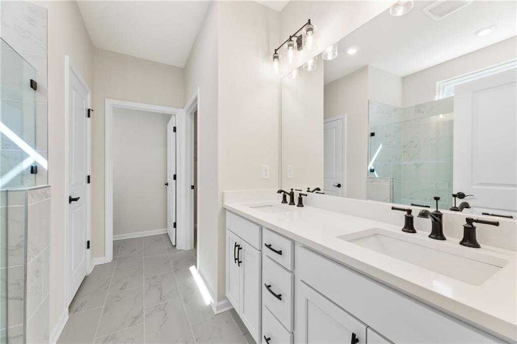 Modern master bathroom featuring double vanity with black faucets, large mirror, and glass shower in Davidson Homes The Daphne B, Loganville, GA