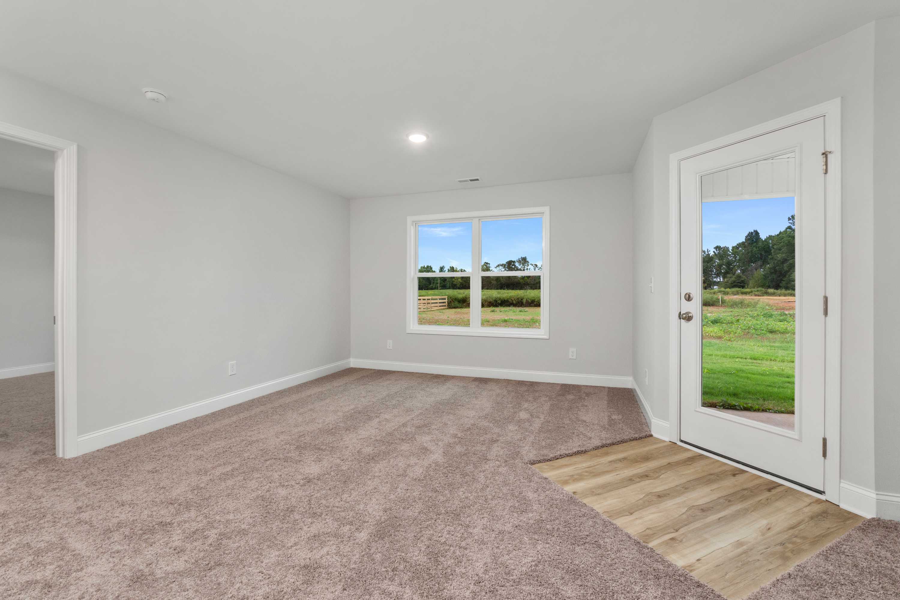 Spacious empty bedroom interior at Collins Lane in Meridianville AL featuring light gray walls, beige carpet, and scenic green field views through large windows