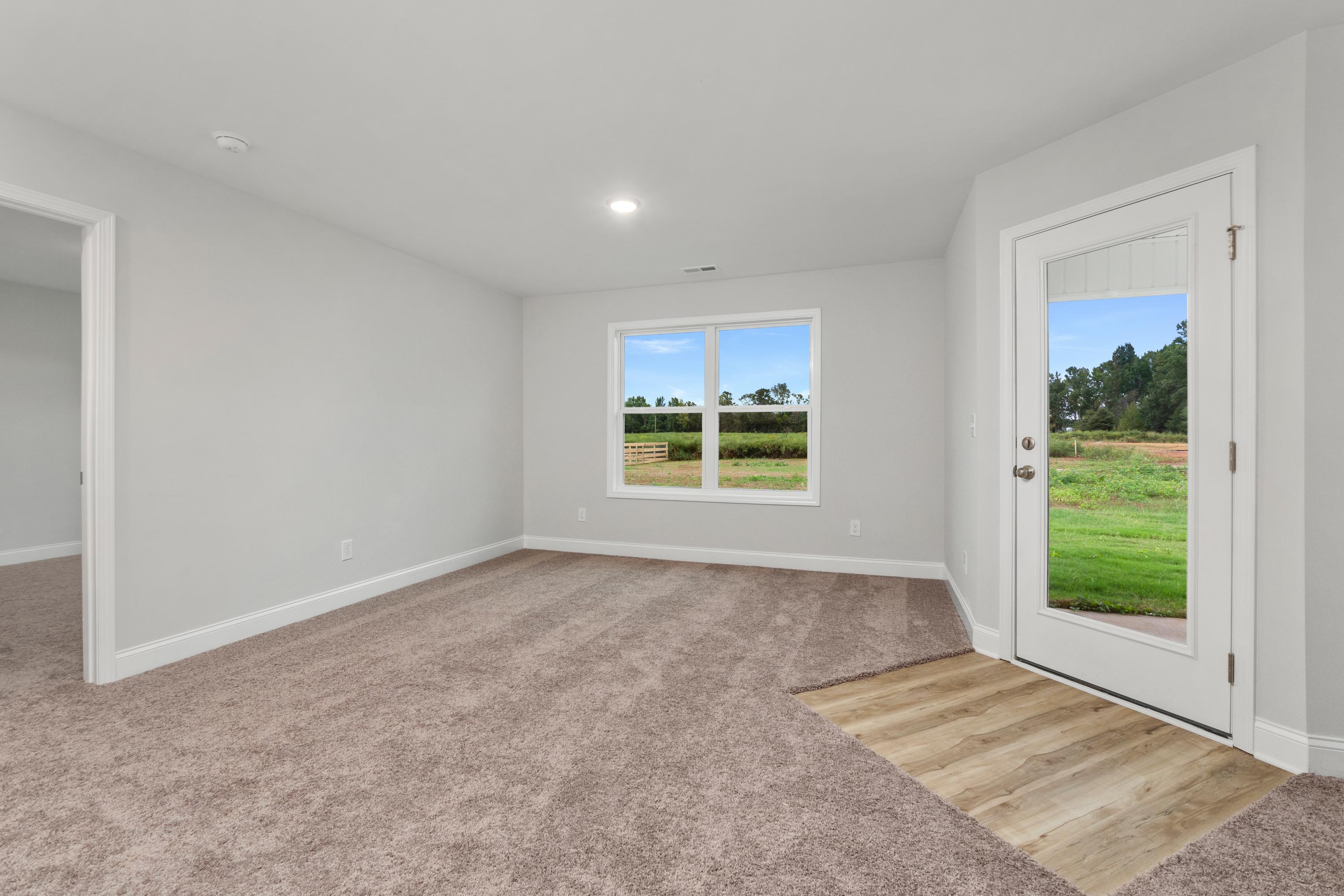 Spacious empty bedroom interior at Collins Lane in Meridianville AL featuring light gray walls, beige carpet, and scenic green field views through large windows