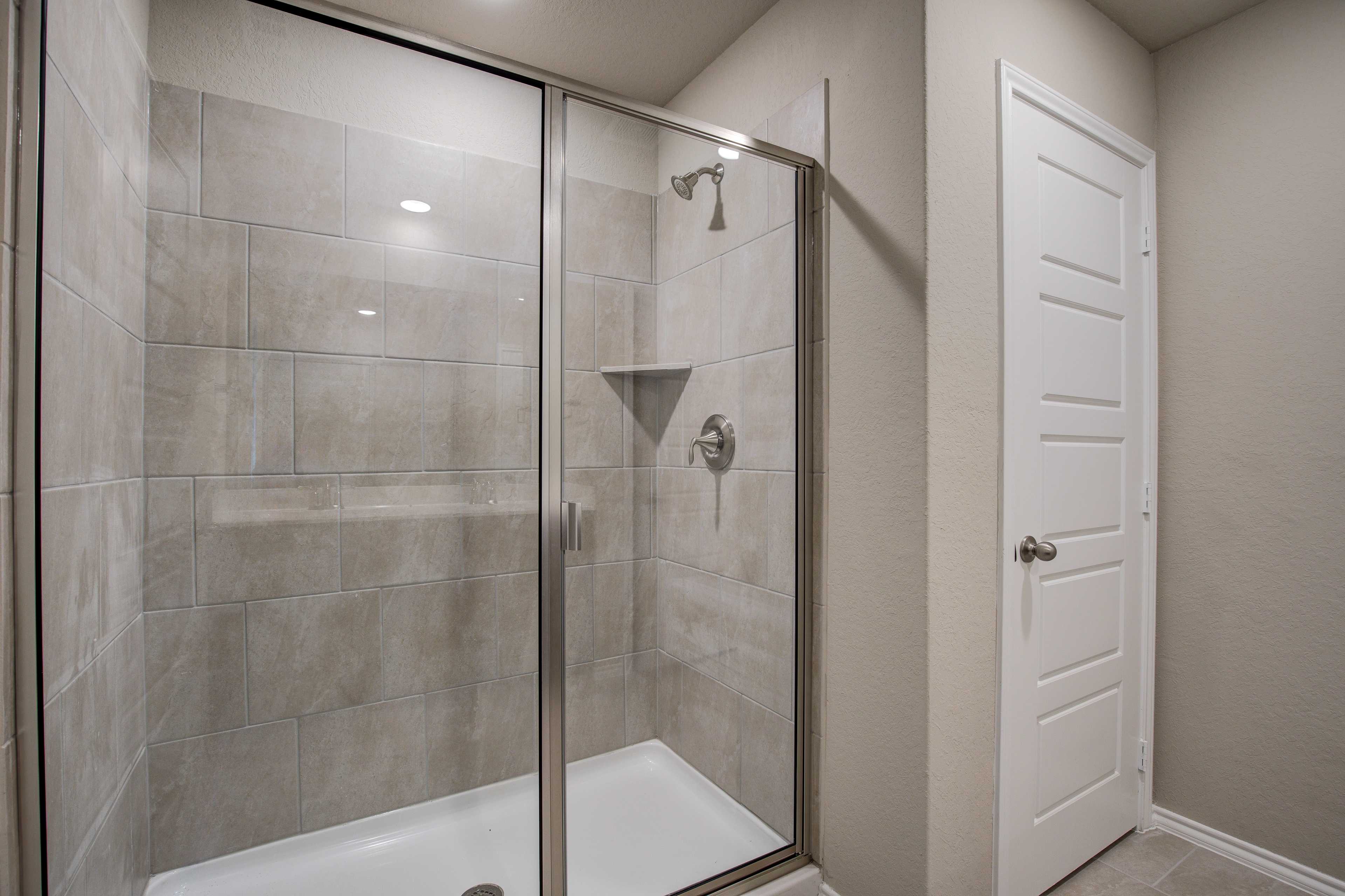 Modern glass-enclosed walk-in shower with gray subway tiles, rain showerhead, and niche in The Murray master bath