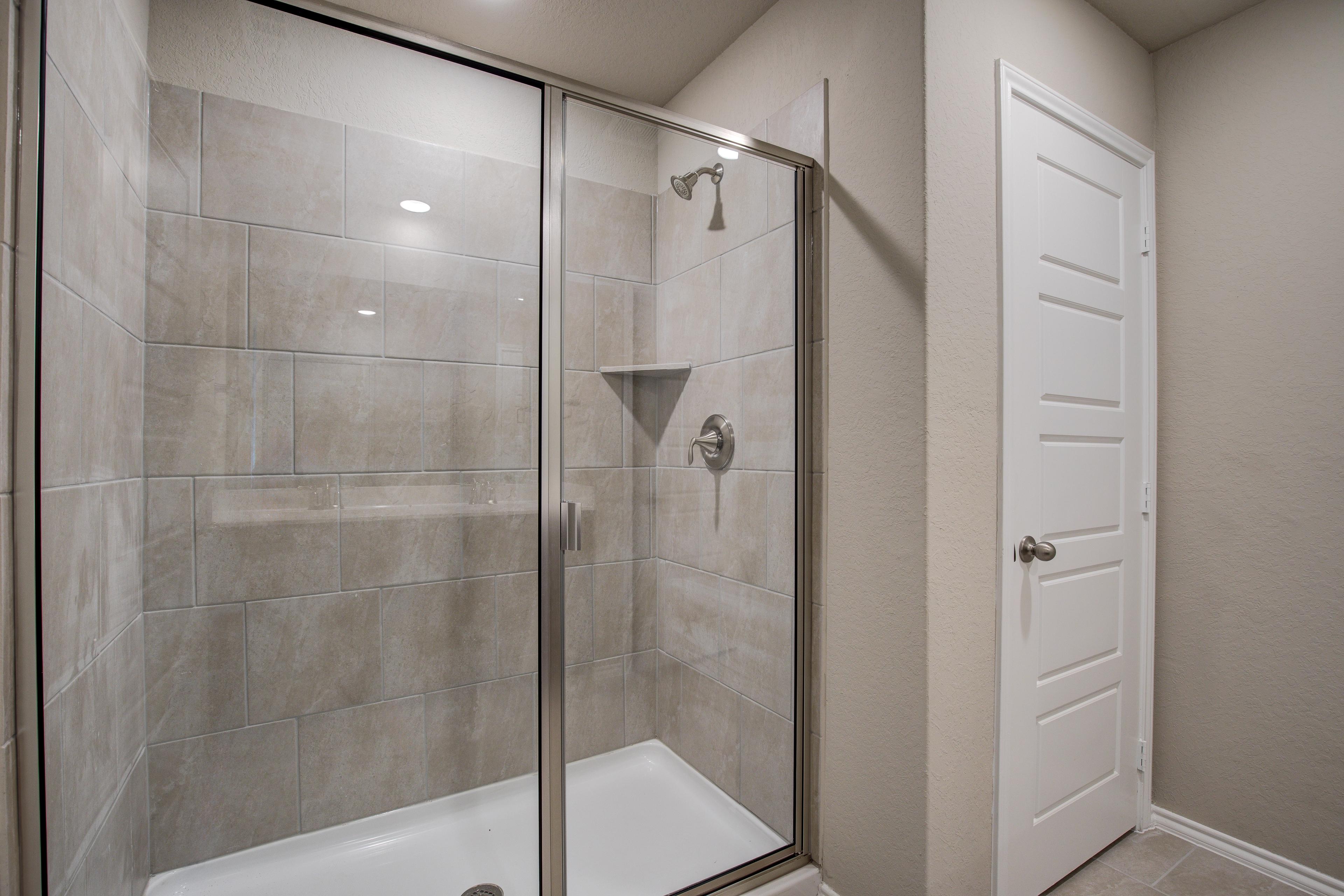 Spacious walk-in shower in The Murray G master bath with frameless glass enclosure, gray subway tiles, and niche shelf