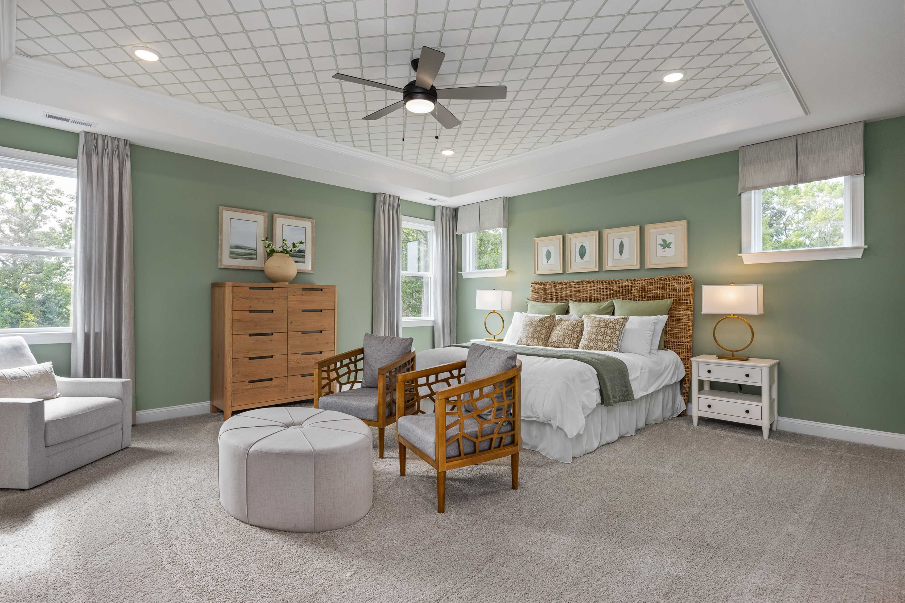 Spacious primary bedroom at Laneridge Estates in Raleigh NC with sage green walls, king bed, armchairs, and ceiling fan