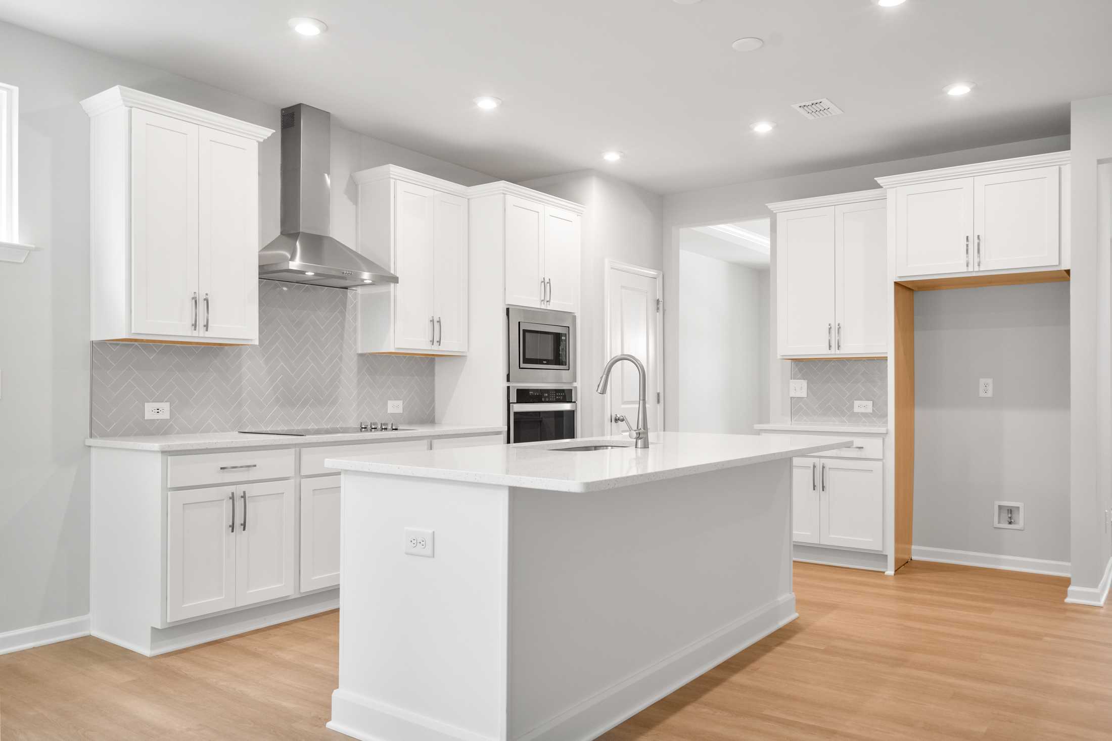 Modern white kitchen in The Ash B featuring large island, stainless steel appliances, subway tile backsplash, and open layout