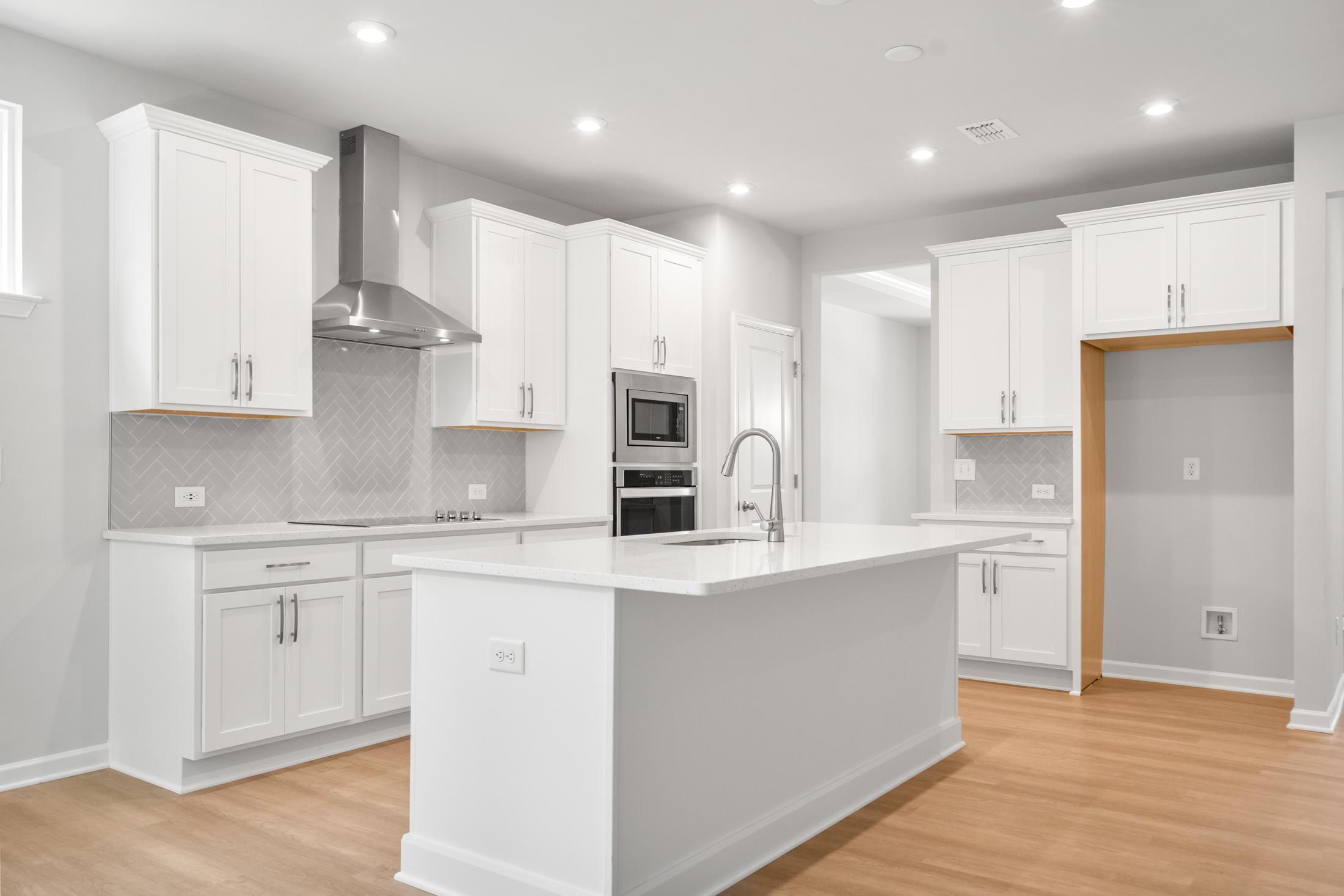 Modern white kitchen in The Ash B featuring large island, stainless steel appliances, subway tile backsplash, and open layout