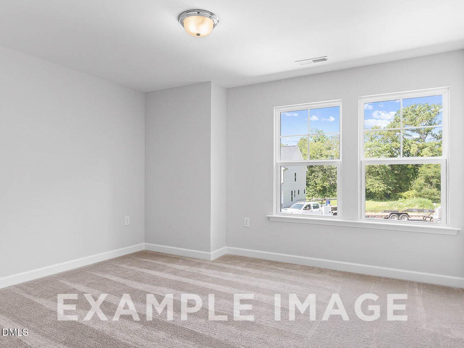 Bright bedroom with light gray walls, large windows overlooking trees and driveway, carpet flooring in Davidson Homes The Chestnut B, Lillington, NC