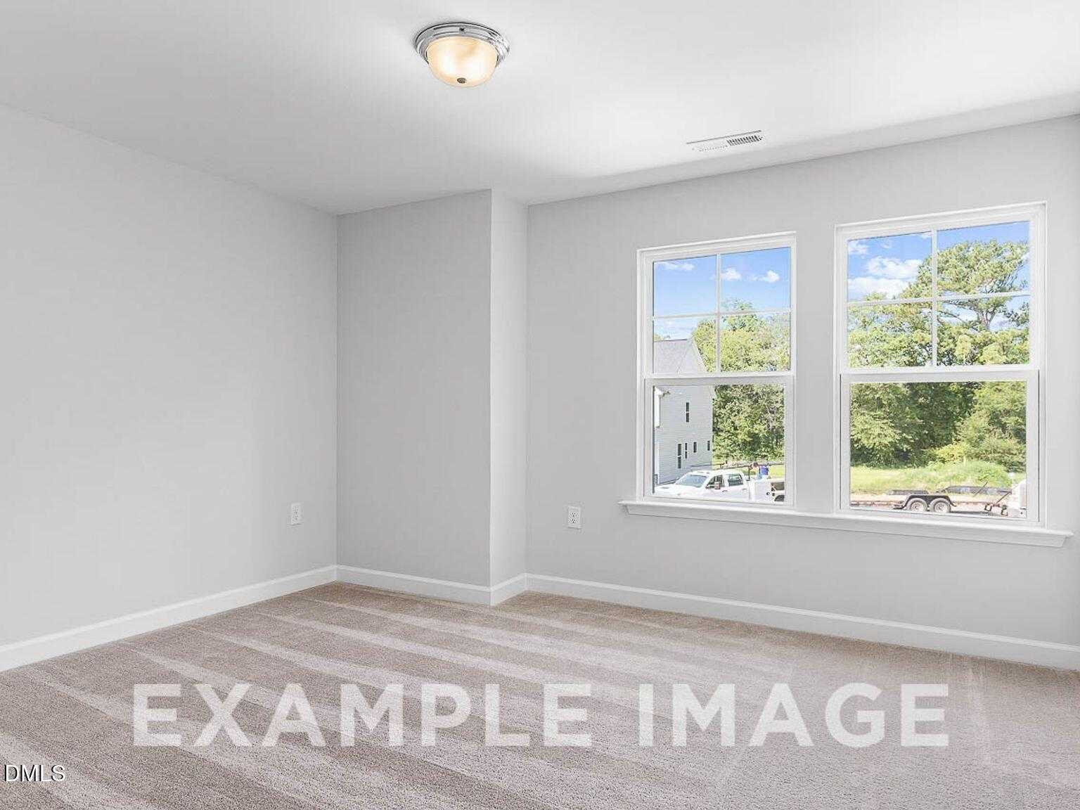 Bright bedroom with light gray walls, carpet floor, and large windows overlooking greenery in Davidson Homes The Chestnut B, Lillington, NC