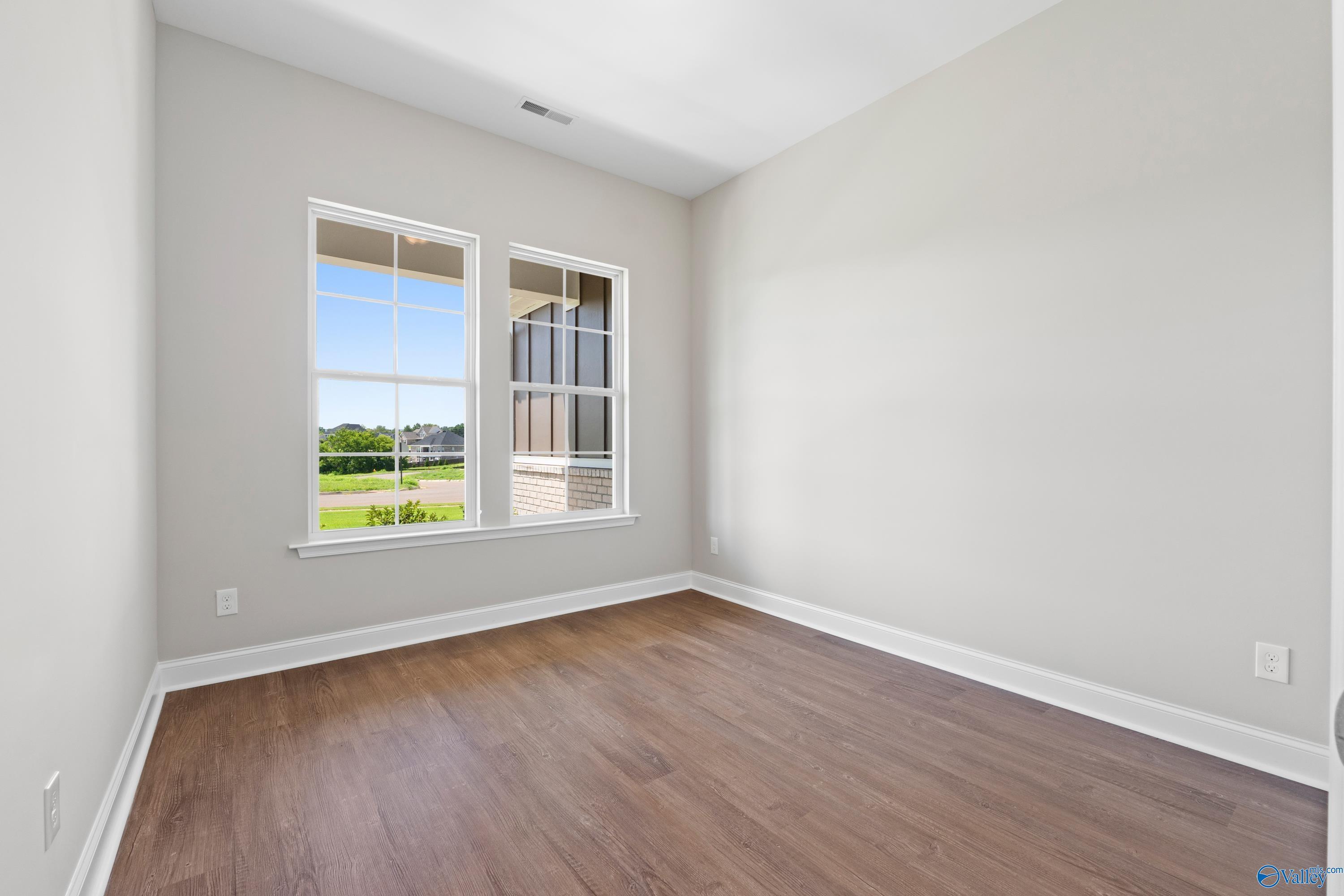 Bright secondary bedroom with large windows overlooking green lawn and hardwood floors in Davidson Homes The Arcadia B, Huntsville, Alabama