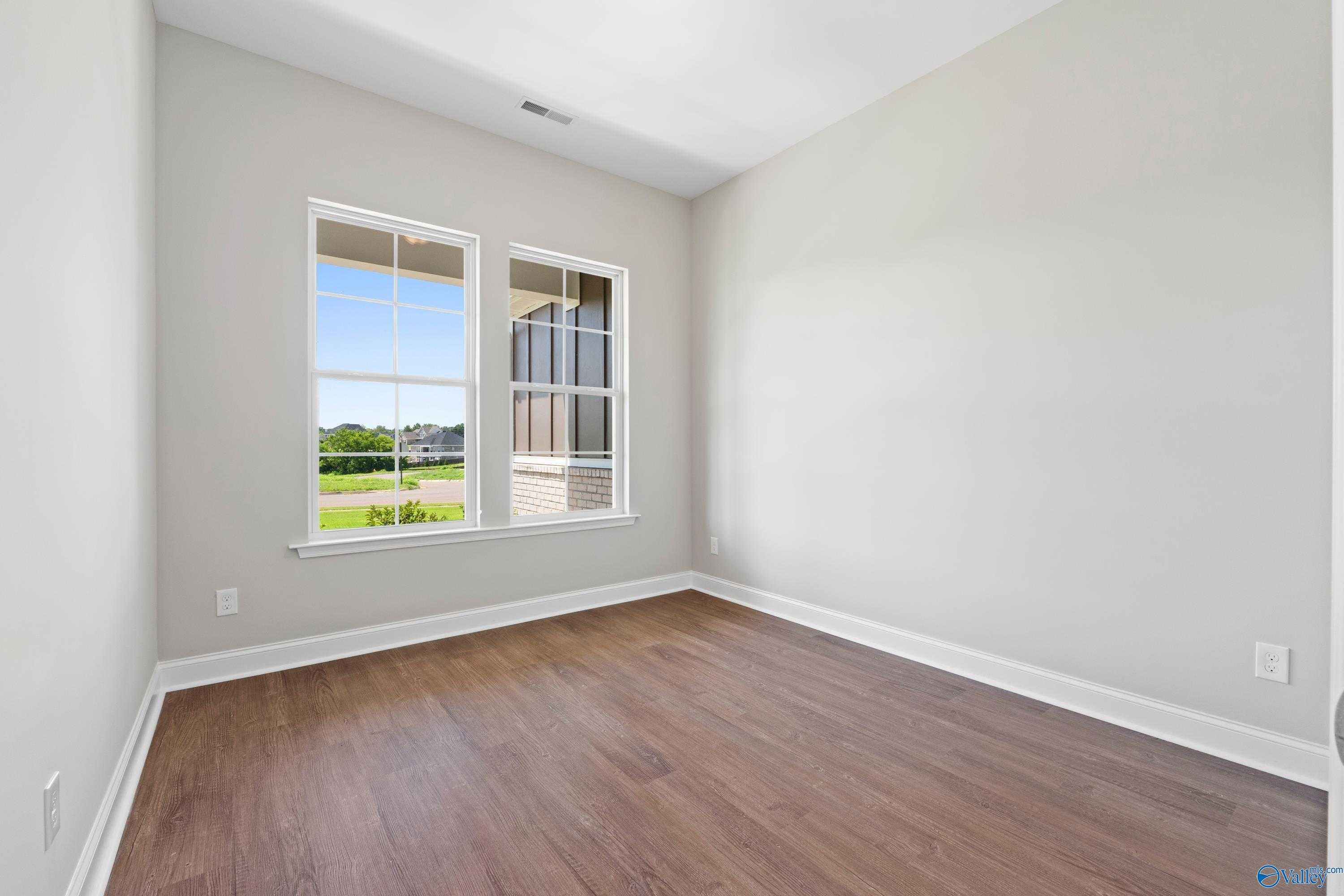 Bright secondary bedroom with large windows overlooking green landscape, hardwood floors in The Arcadia home, Huntsville, Alabama