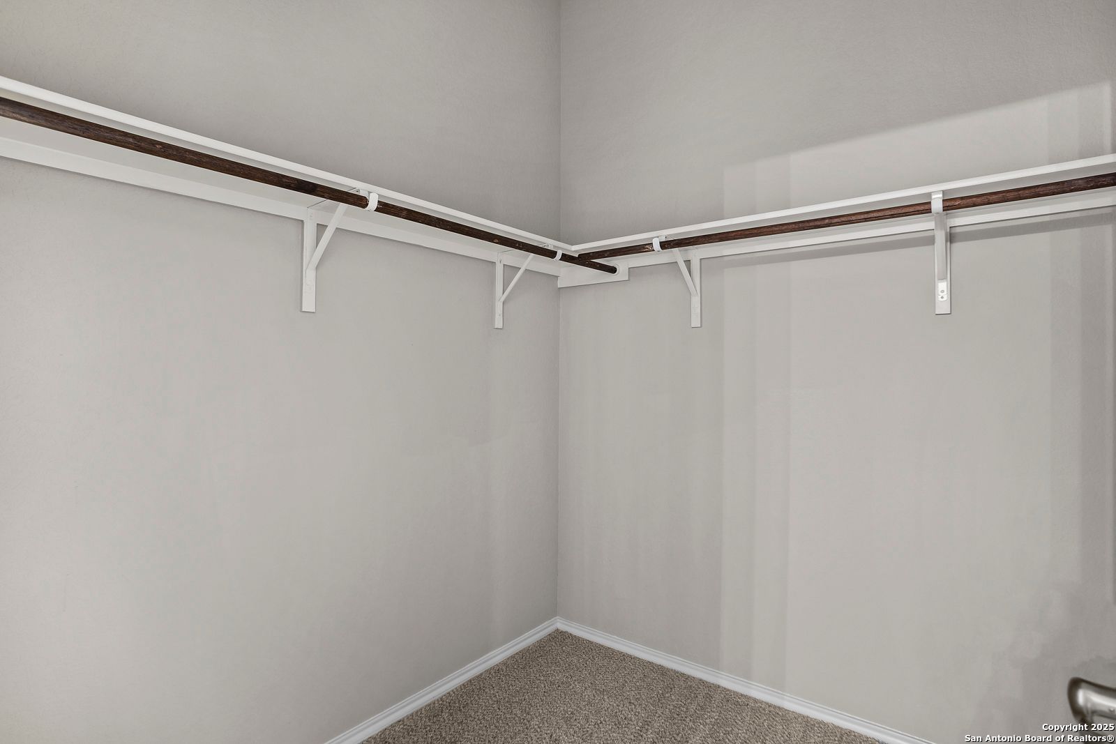 Spacious walk-in closet with double wood hanging rods and carpeted floor in Davidson Homes The Collin B, Seguin, Texas