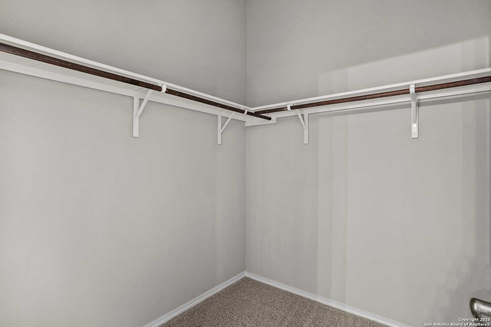 Spacious walk-in closet with double wood hanging rods and carpeted floor in Davidson Homes The Collin B, Seguin, Texas