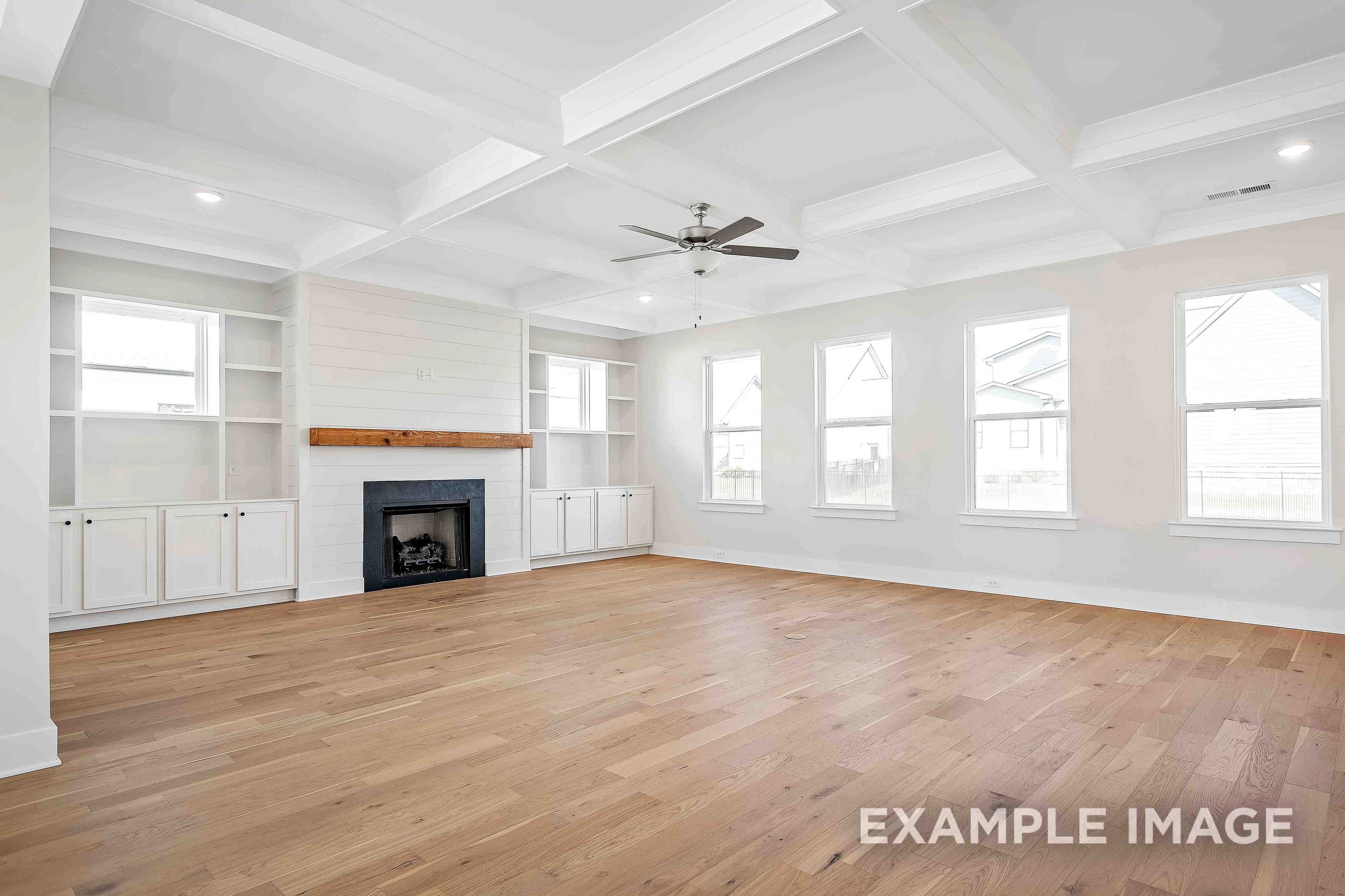 Spacious great room in The Alston A with hardwood floors, shiplap fireplace wall, coffered ceiling, and large windows