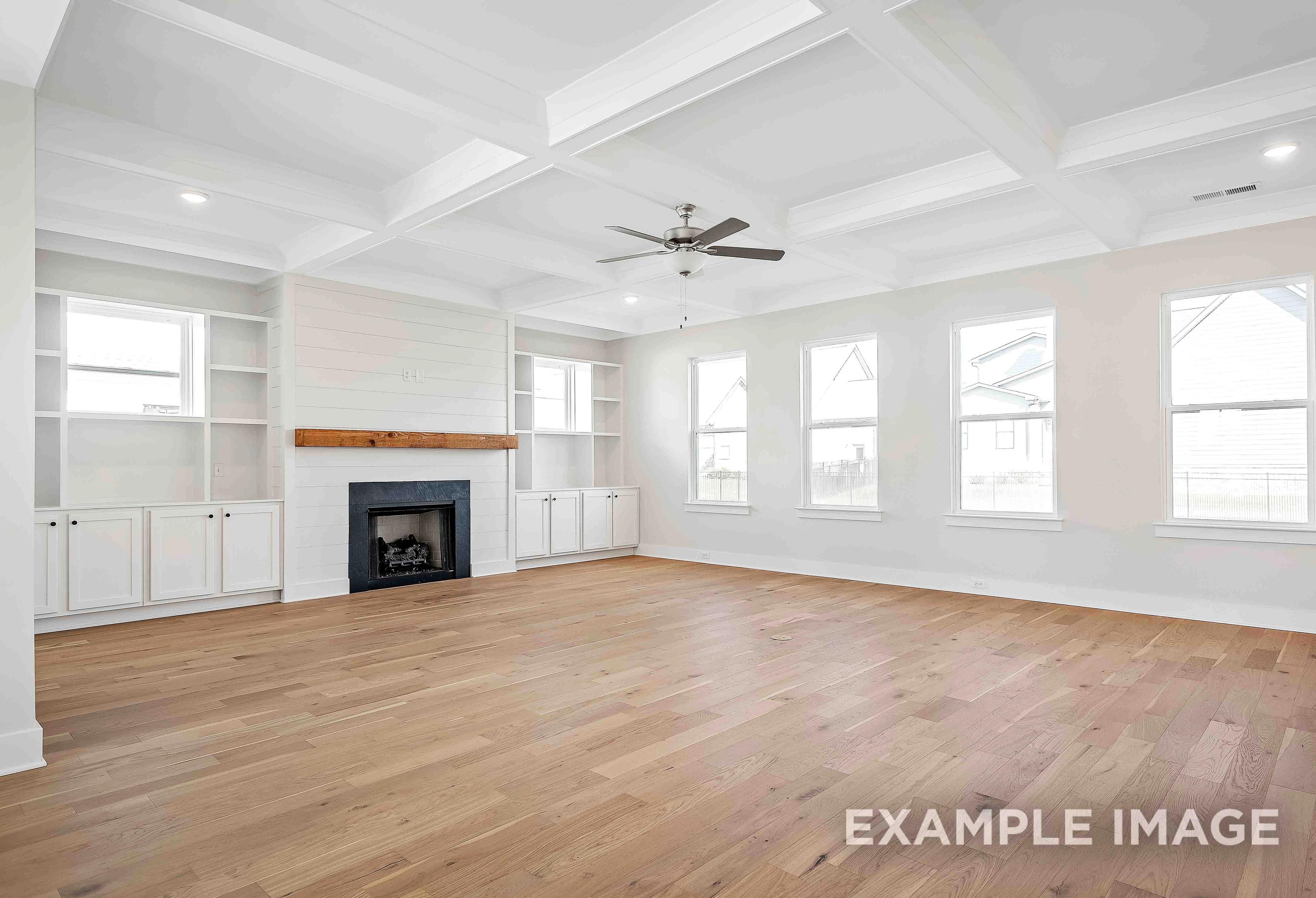 Spacious great room in The Alston A with hardwood floors, shiplap fireplace wall, coffered ceiling, and large windows