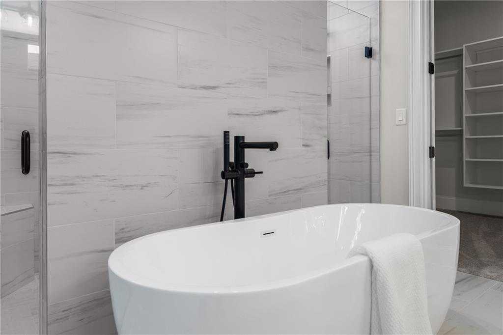 Luxurious master bathroom featuring freestanding soaking tub, black faucet, and frameless glass shower in Davidson Homes Seaside B, Woodstock, Georgia