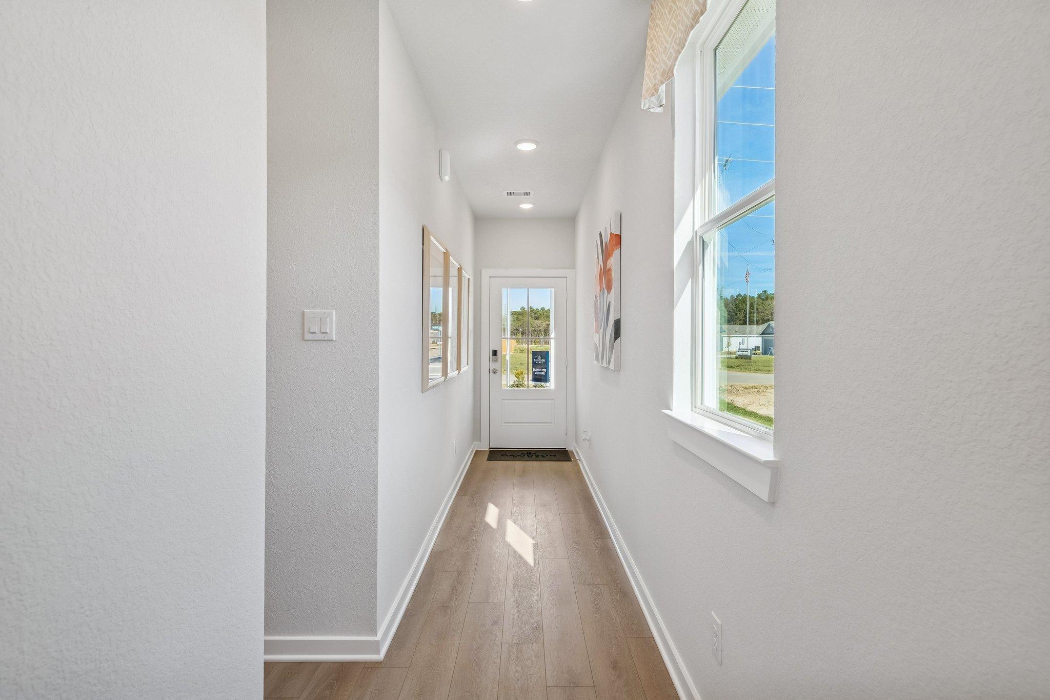 Spacious hallway interior at Spring Branch Crossing in Conroe Texas with light hardwood floors, white walls, and scenic window view