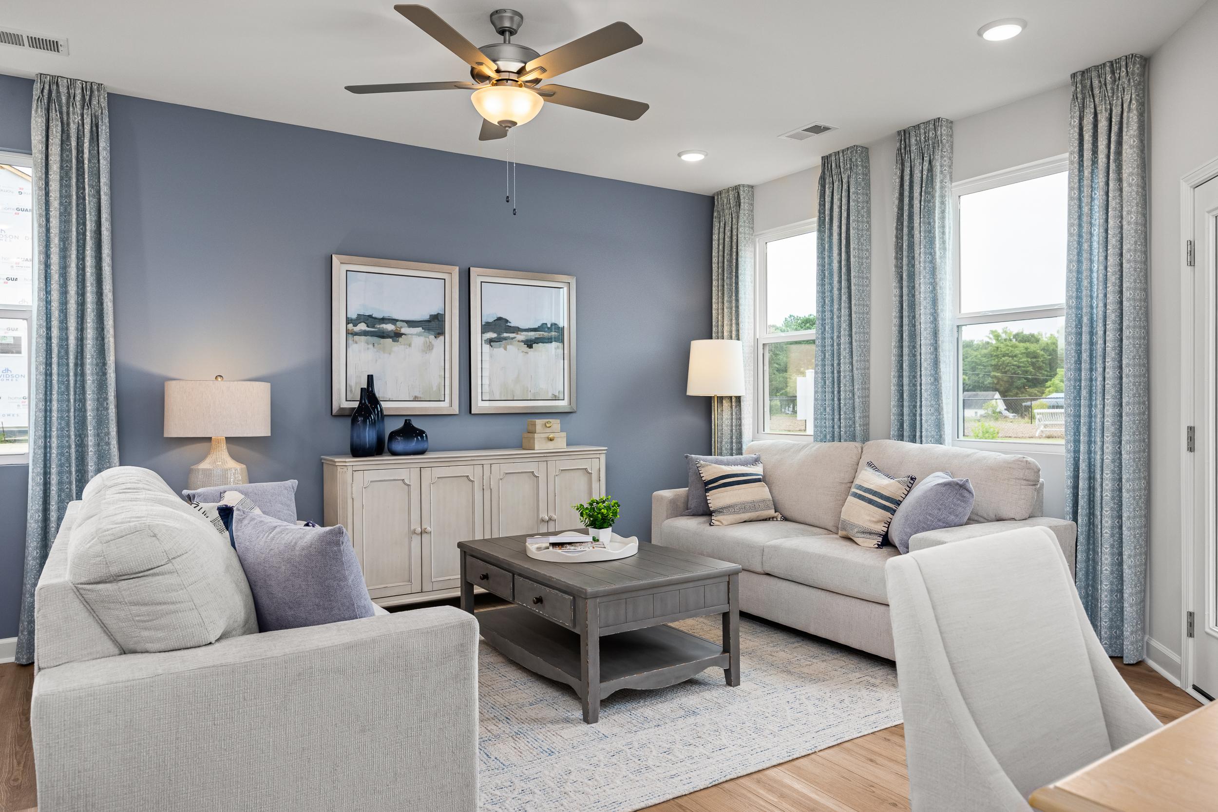 Cozy living room in Springvale Fuquay-Varina NC with blue walls white sofas hardwood floors and ceiling fan by Davidson Homes