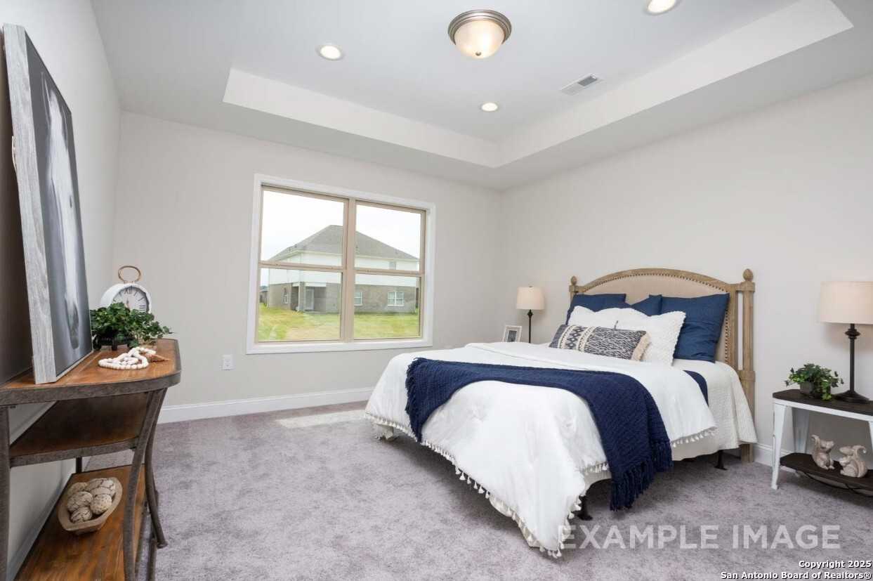Inviting secondary bedroom with neutral walls, king bed in white duvet, large window view, and modern decor in Davidson Homes The Asheville K, Bricewood, San Antonio