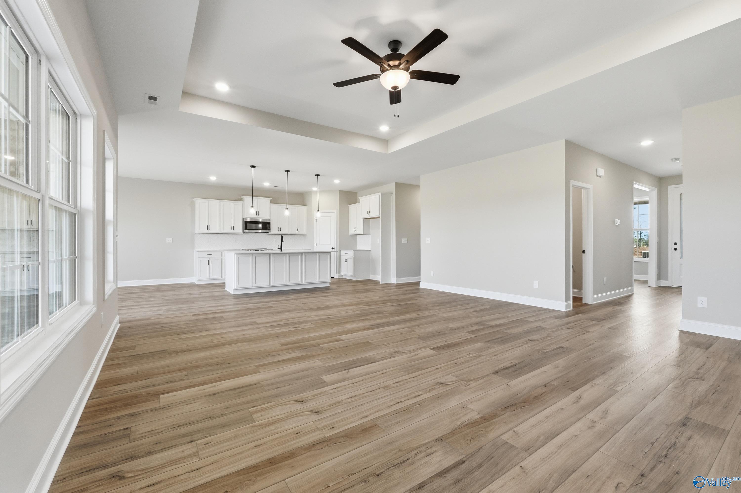 Open-concept kitchen and living space with white island, cabinets, hardwood floors, ceiling fan in Davidson Homes The Rockford, Harvest, AL
