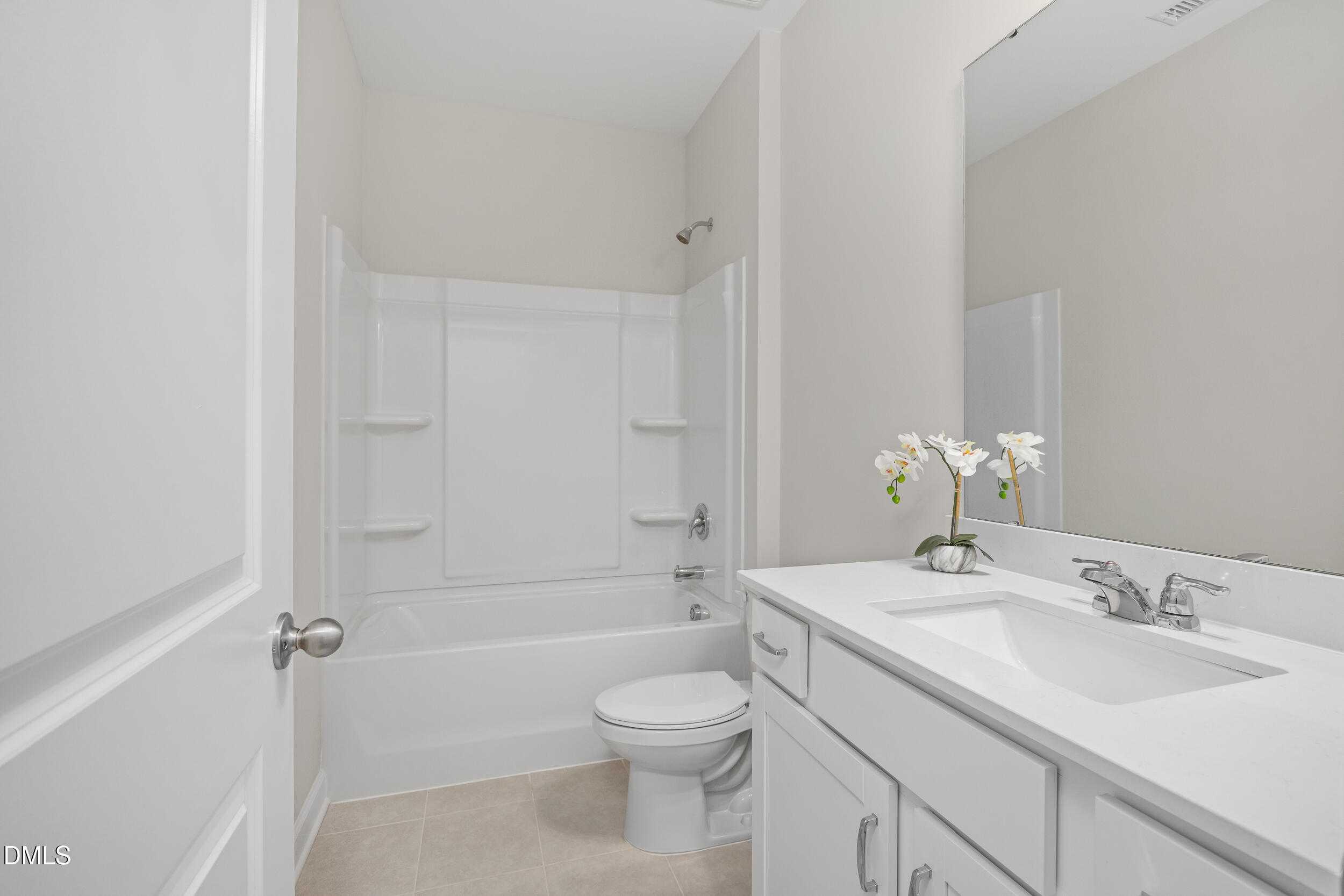 Modern guest bathroom featuring white tub, shower, vanity sink, and orchids in Davidson Homes The Preston C, Lillington, NC