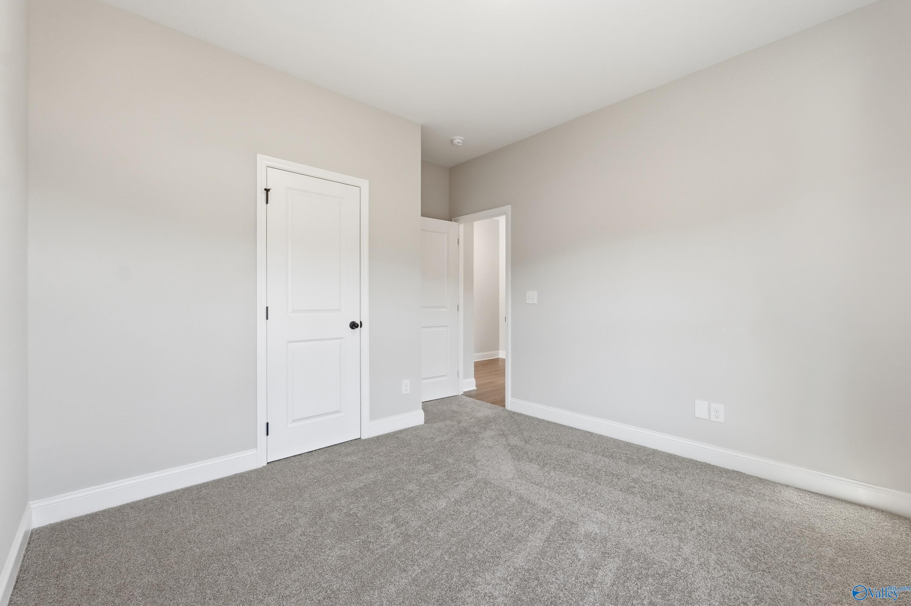 Spacious empty bedroom with gray carpet, beige walls, and white doors in Davidson Homes The Franklin E, Hazel Green, Alabama