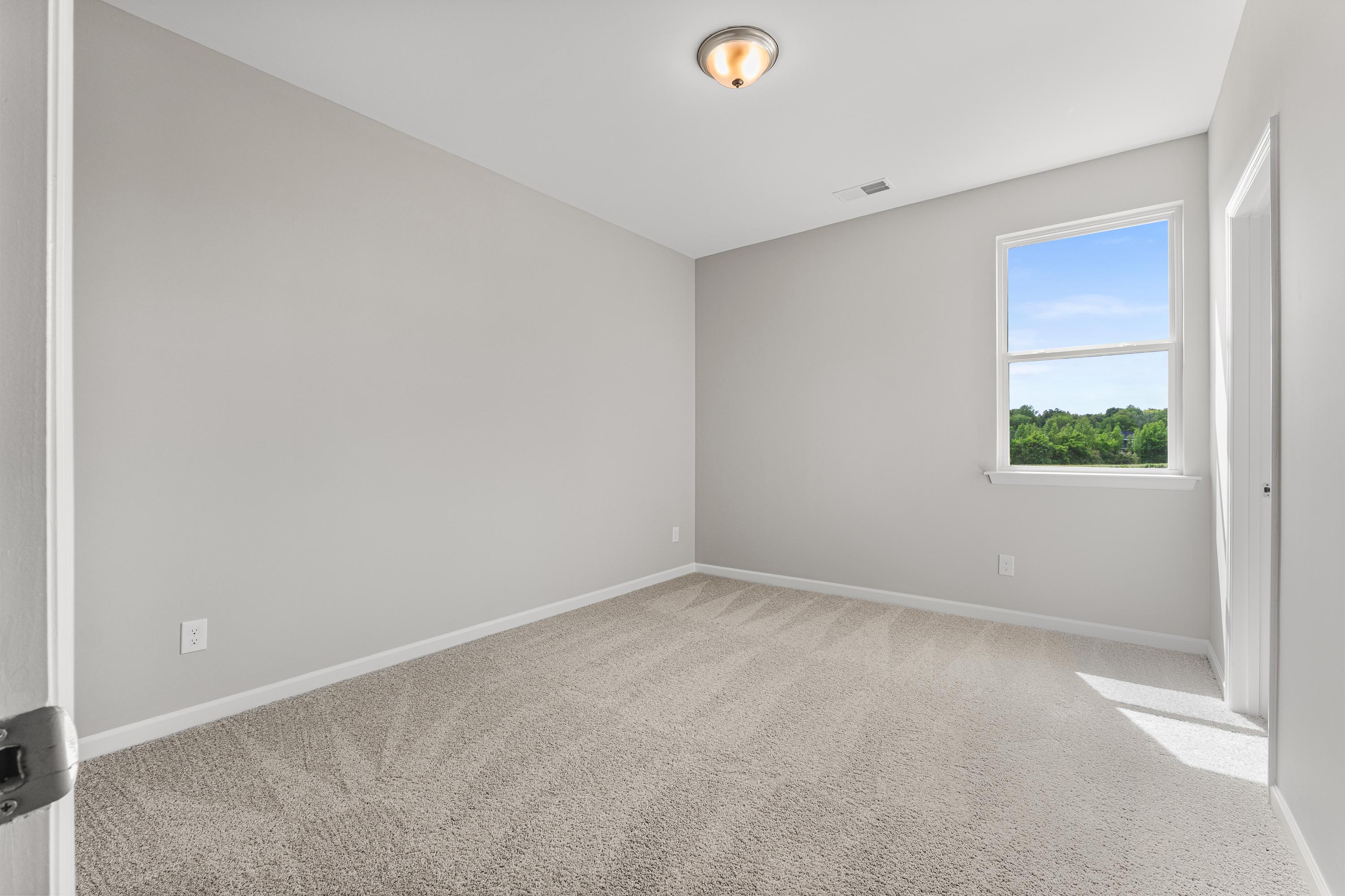 Spacious empty bedroom in The Haven E featuring light gray walls, beige carpet, ceiling light, and window with green view