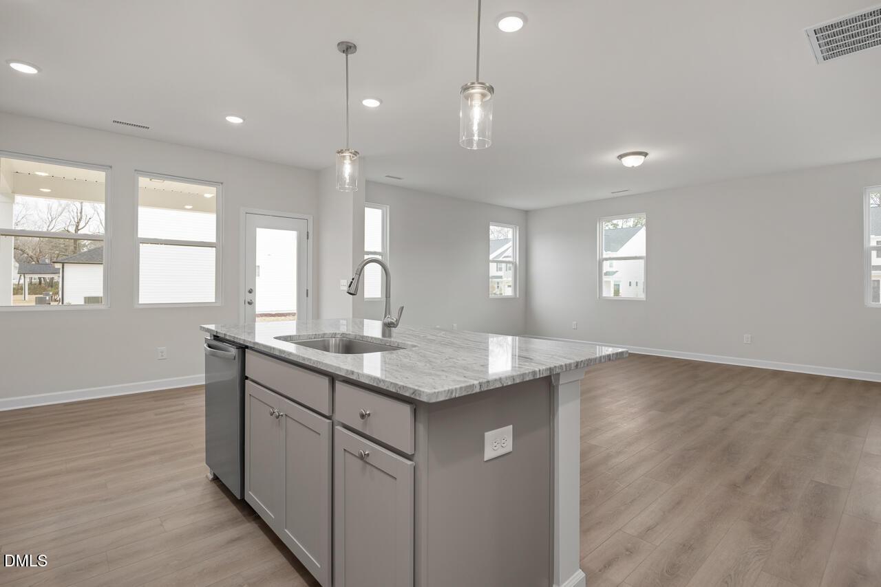 Modern open-concept kitchen with granite island, stainless sink, gray cabinets, and large windows in The Gavin B, Lillington, NC