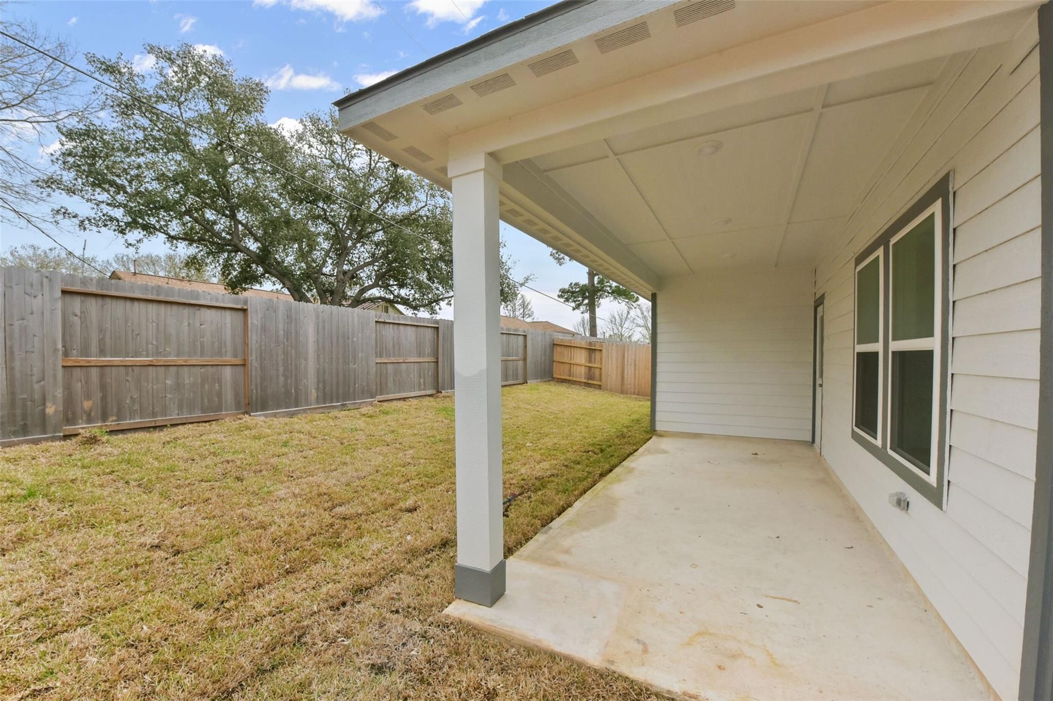 Covered back patio with wooden fence and green lawn in Davidson Homes The Laguna B, Windmill Estates, Magnolia, Texas