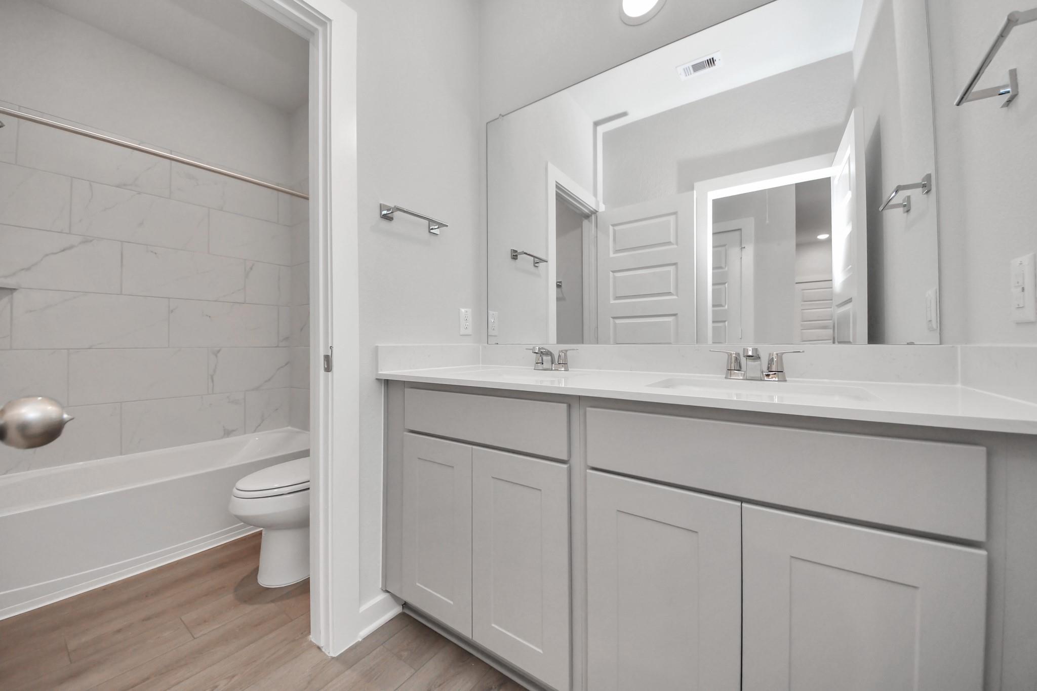 Modern bathroom with double vanity and tiled tub-shower combo in The Colorado G floor plan at Emberly in Beasley, Texas.
