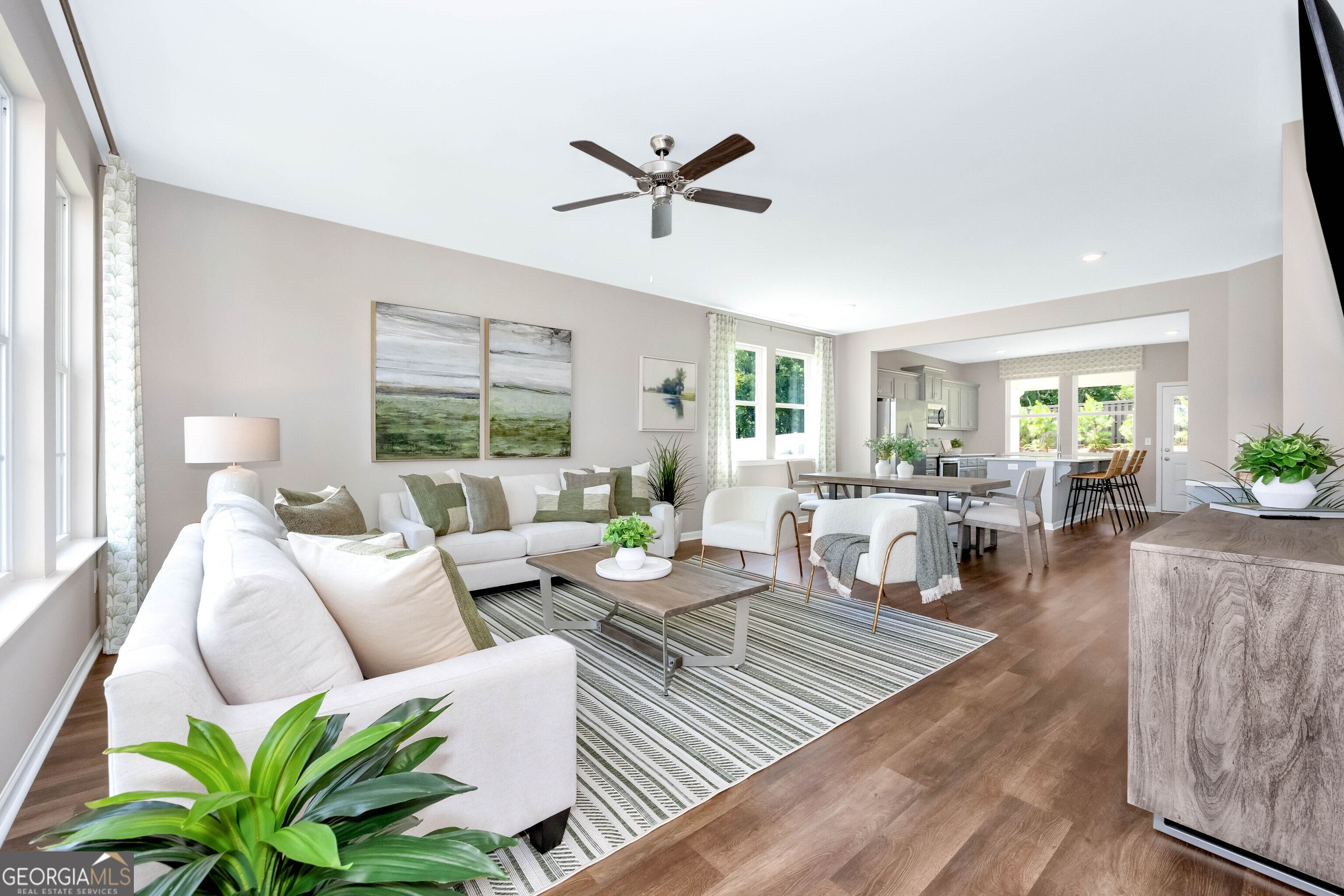 Bright open living-dining area with white sectional sofa, ceiling fan, plants, and hardwood floors in Evermore Homes The Stella, Perry, Georgia