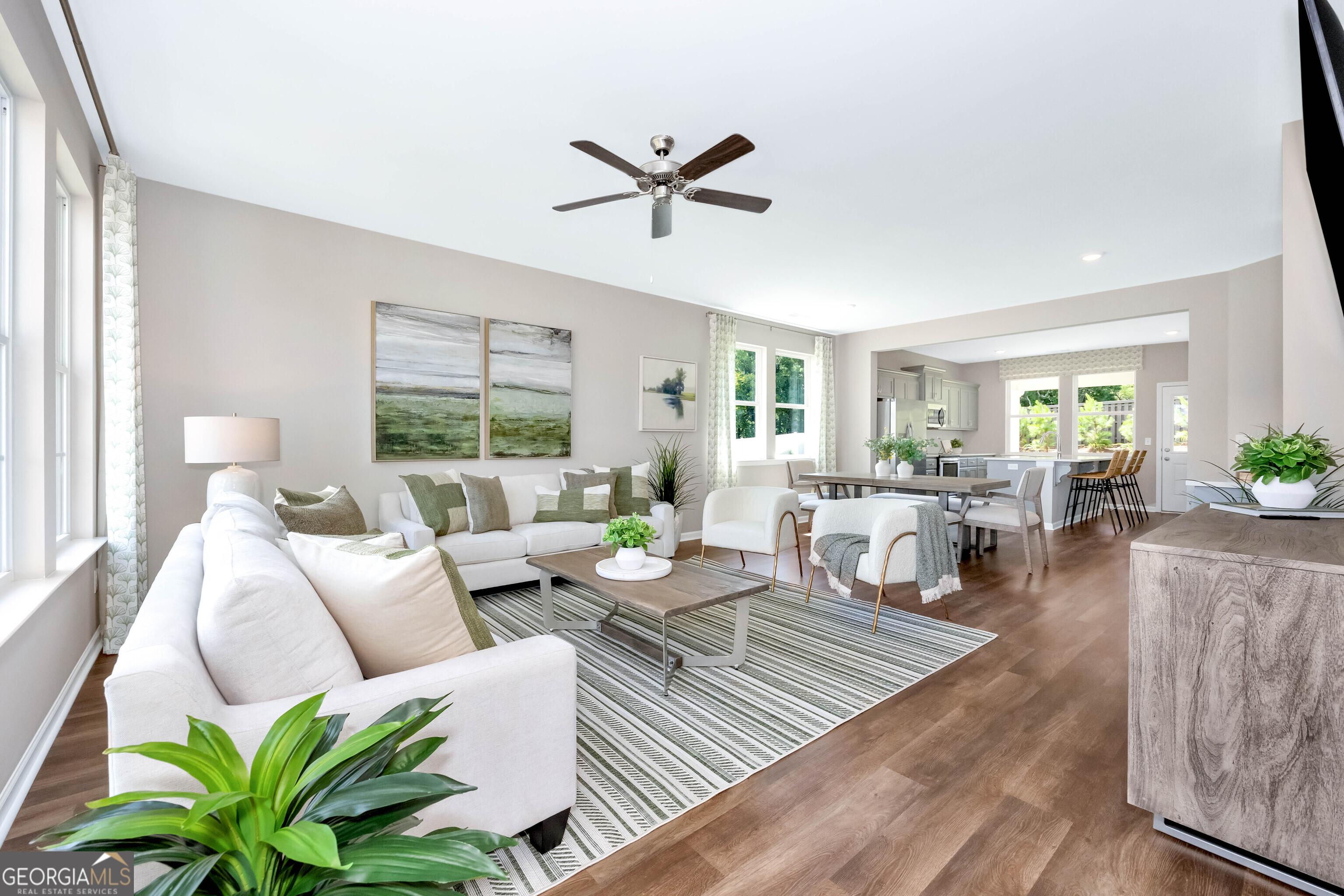 Bright open living-dining area with white sectional sofa, ceiling fan, plants, and hardwood floors in Evermore Homes The Stella, Perry, Georgia