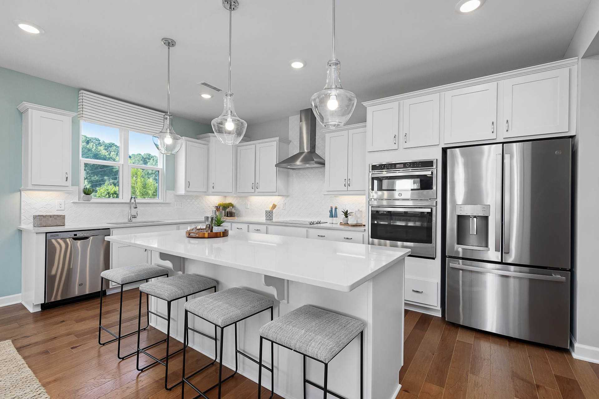 Spacious white kitchen at Bentwinds in Fuquay-Varina NC with quartz island, stainless appliances, pendant lights, hardwood floors