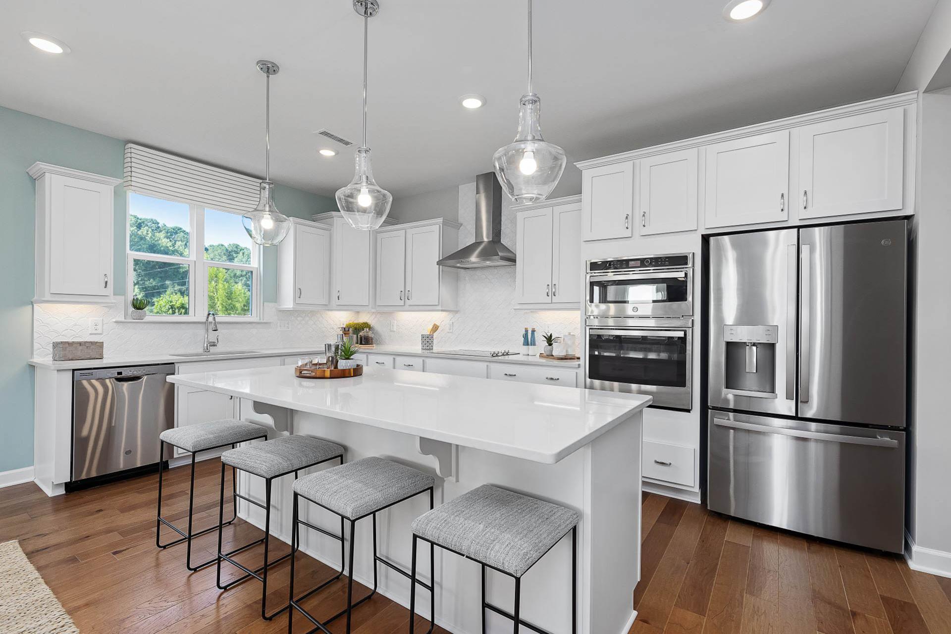 Spacious white kitchen at Bentwinds in Fuquay-Varina NC with quartz island, stainless appliances, pendant lights, hardwood floors