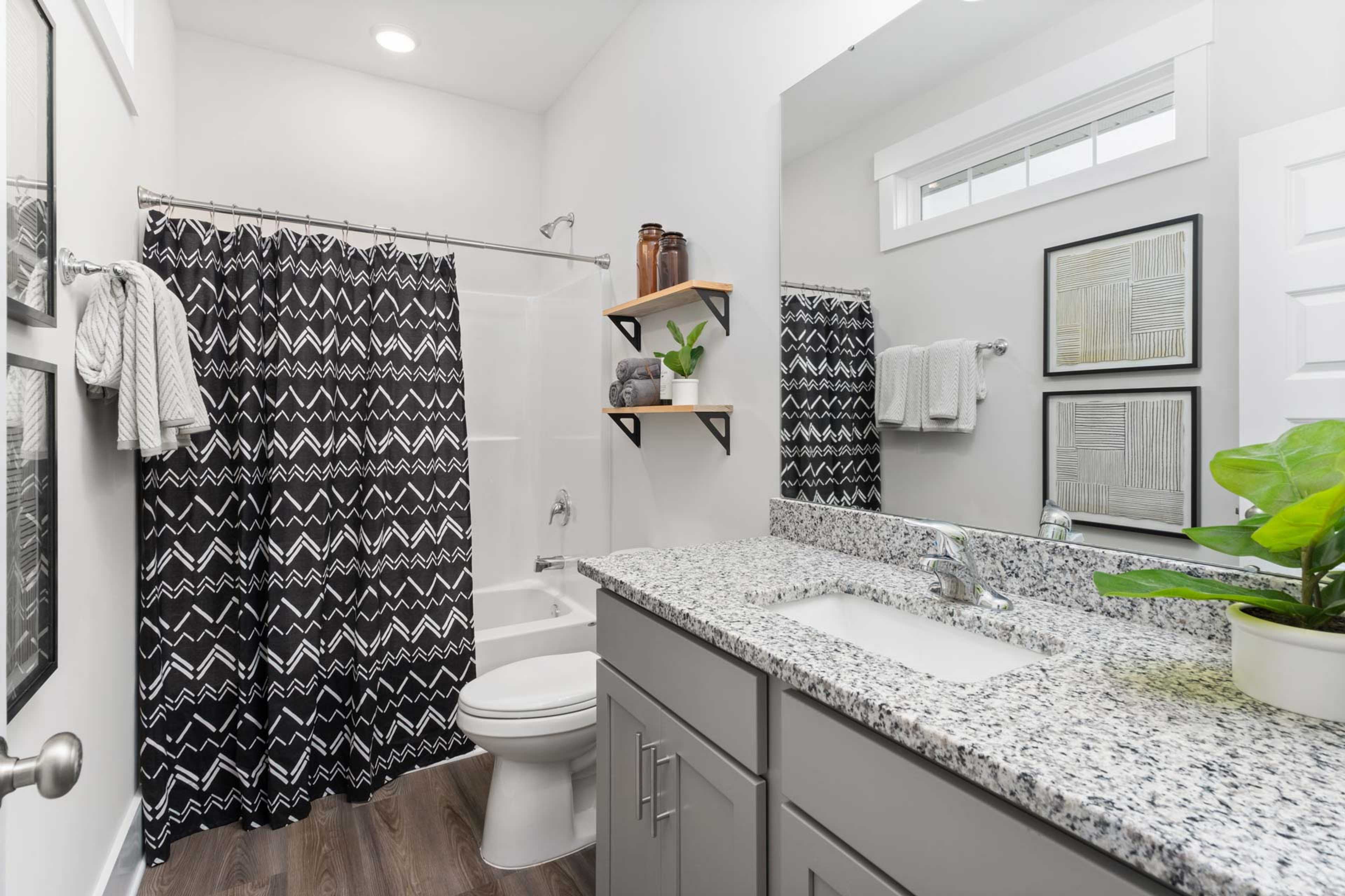 Modern bathroom at The Meadows in Athens AL with black patterned shower curtain, freestanding tub, quartz vanity, and plants