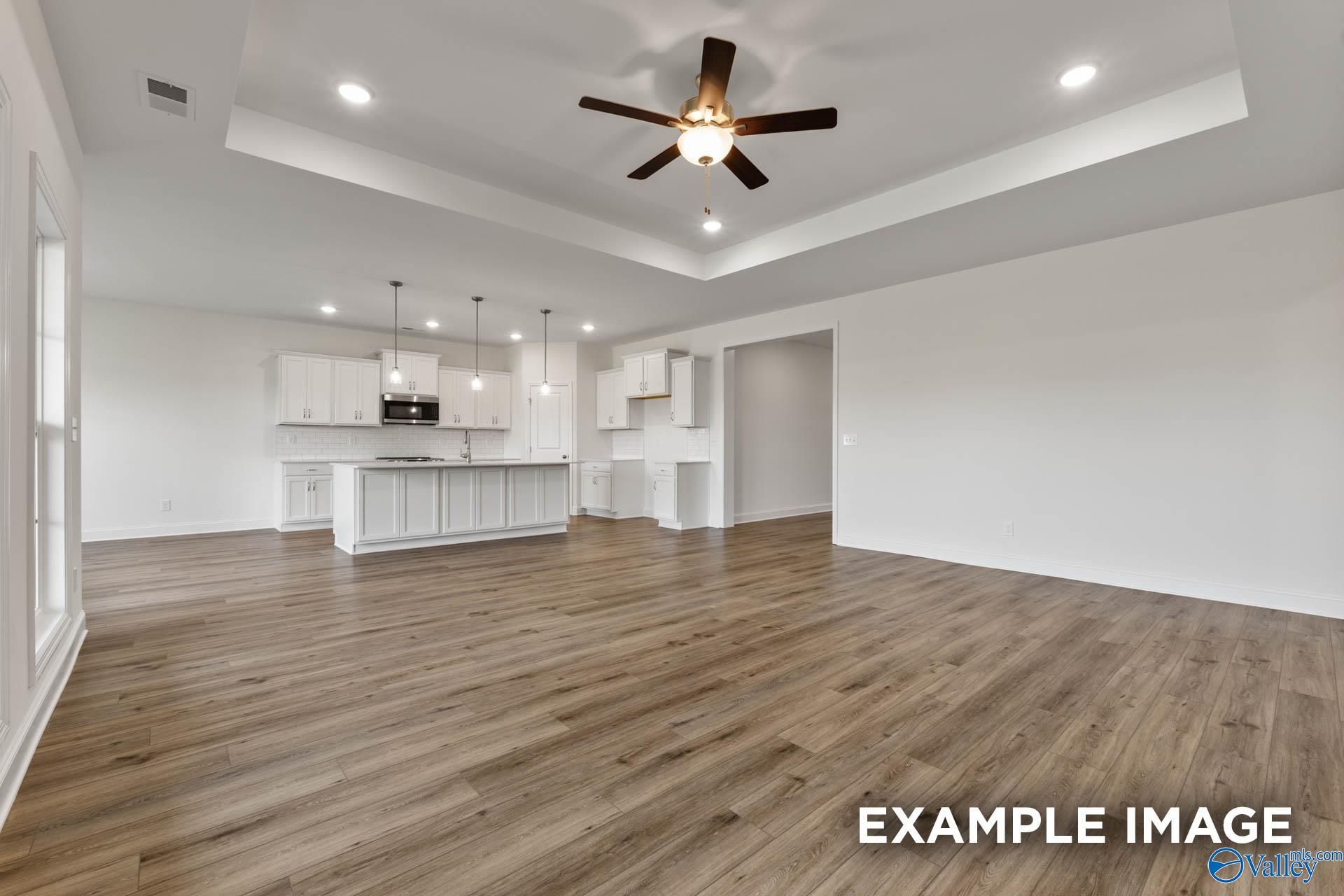 Bright open-concept kitchen with white cabinets, large island, and living area featuring hardwood floors in Davidson Homes Harrison C, Athens AL