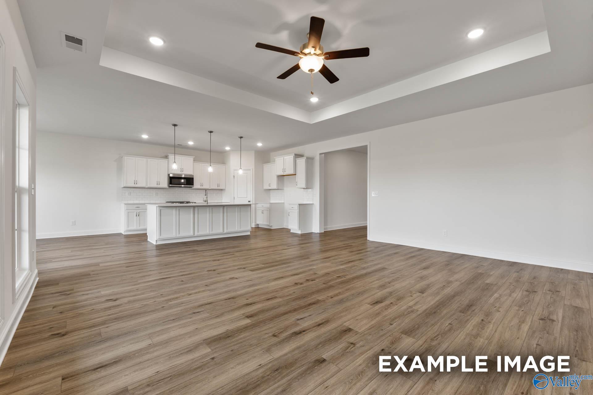 Bright open-concept kitchen with white cabinets, large island, and living area featuring hardwood floors in Davidson Homes Harrison C, Athens AL