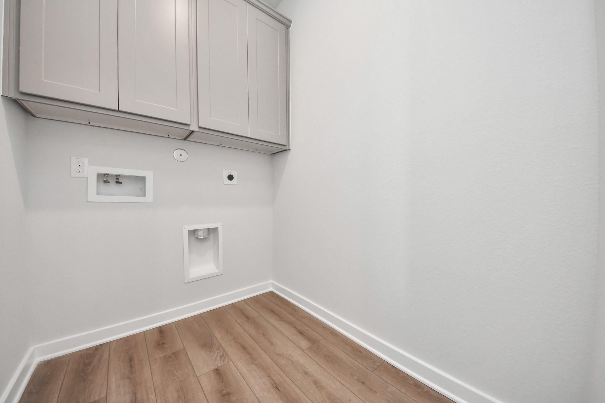 Laundry room with grey upper cabinets and wood-look flooring in The Riviera A floor plan at Emberly in Beasley, Texas.