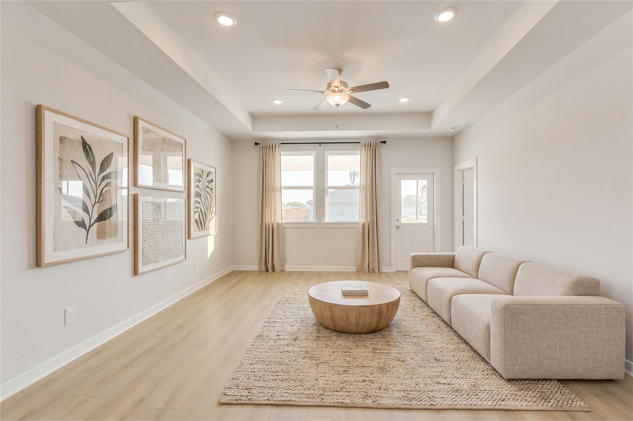 Bright living room with neutral walls, ceiling fan, large windows, beige sectional sofa, wooden coffee table on jute rug in The Frio G, Conroe Texas