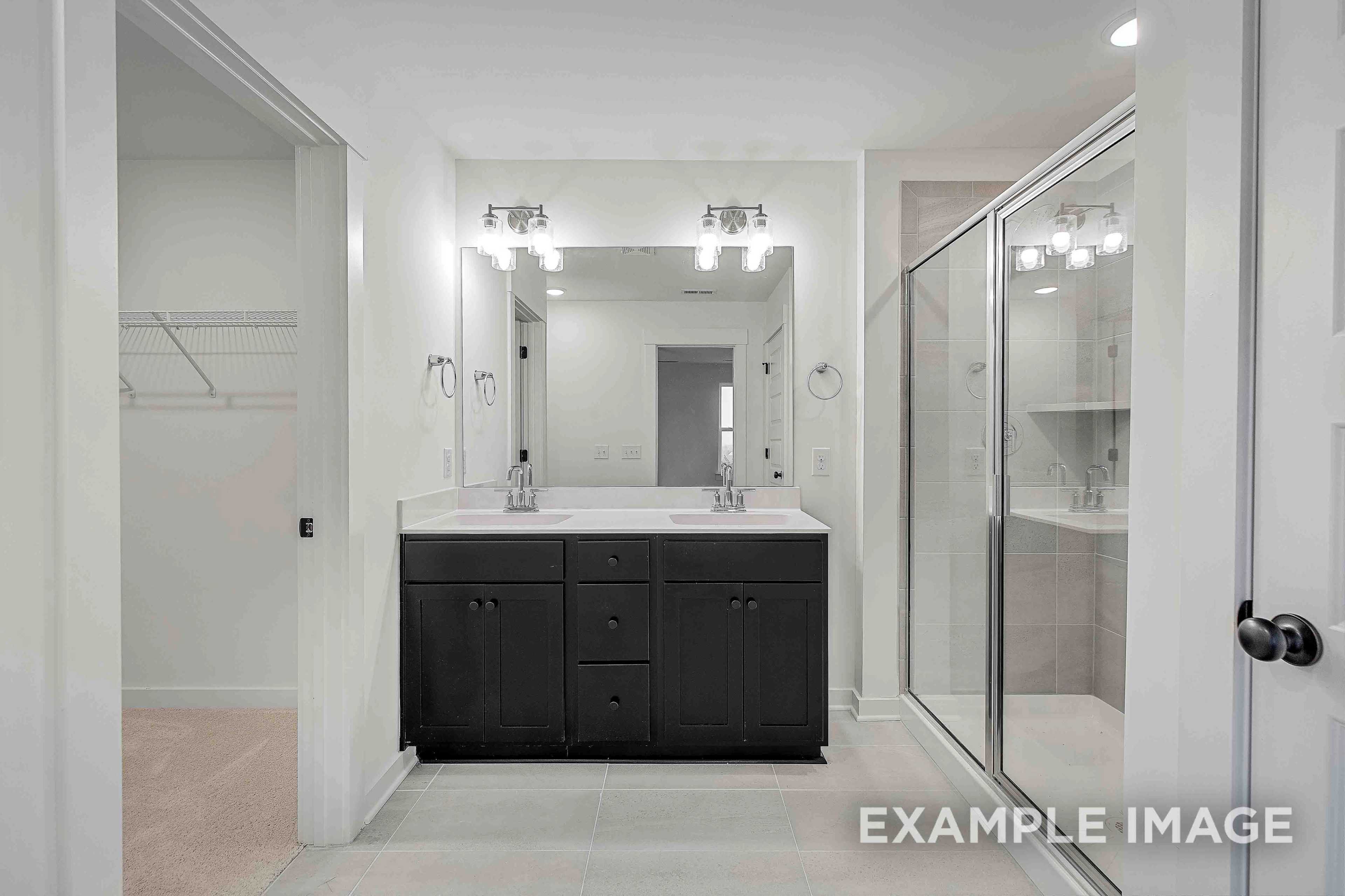 Spacious master bathroom in The Charleston with dark double vanity, glass walk-in shower, and adjacent closet