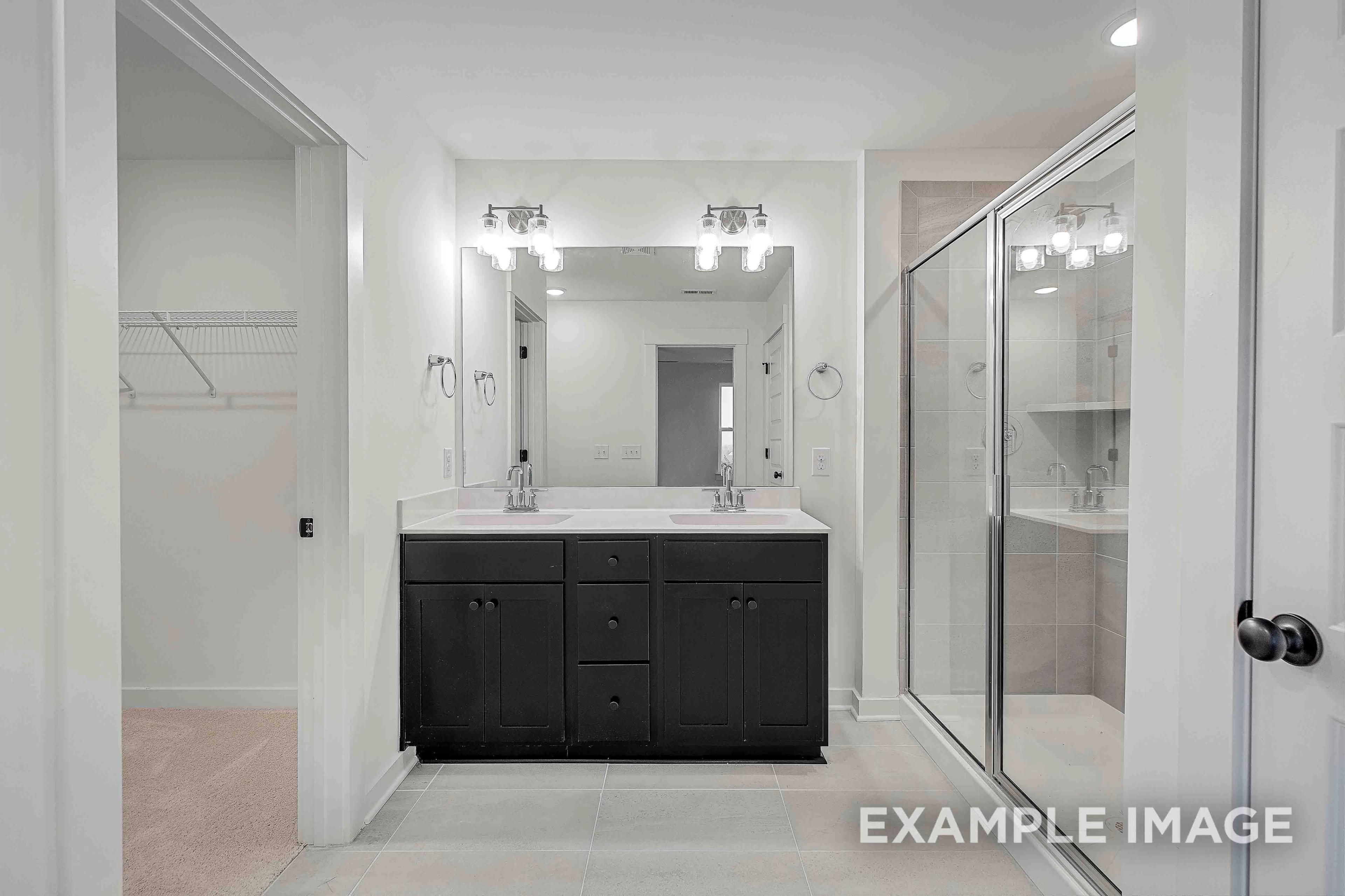 Spacious master bathroom in The Charleston with dark double vanity, glass walk-in shower, and adjacent closet