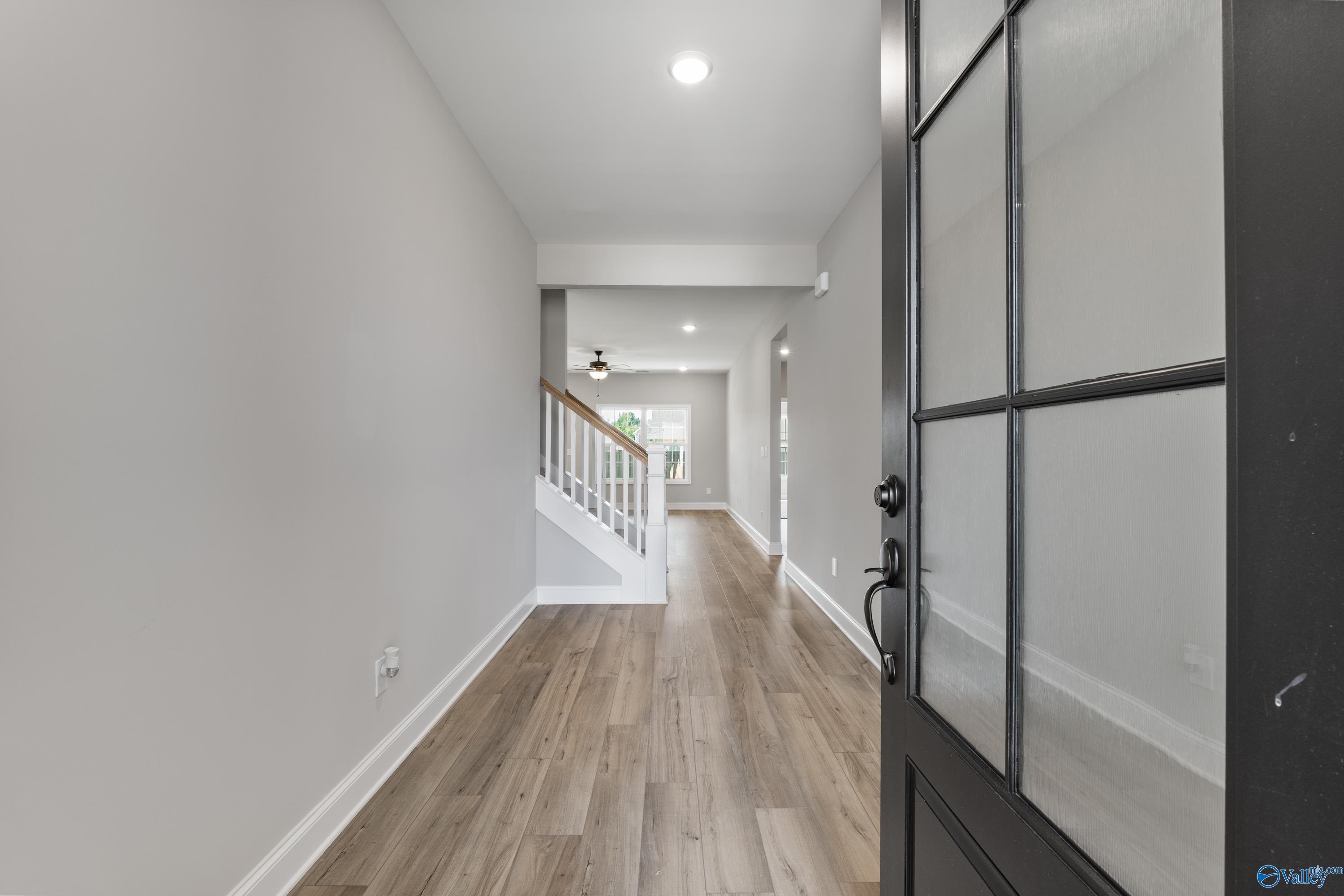 Bright entry hallway with light gray walls, oak hardwood floors, and white staircase in The Montgomery B With Bonus by Davidson Homes, Toney, Alabama