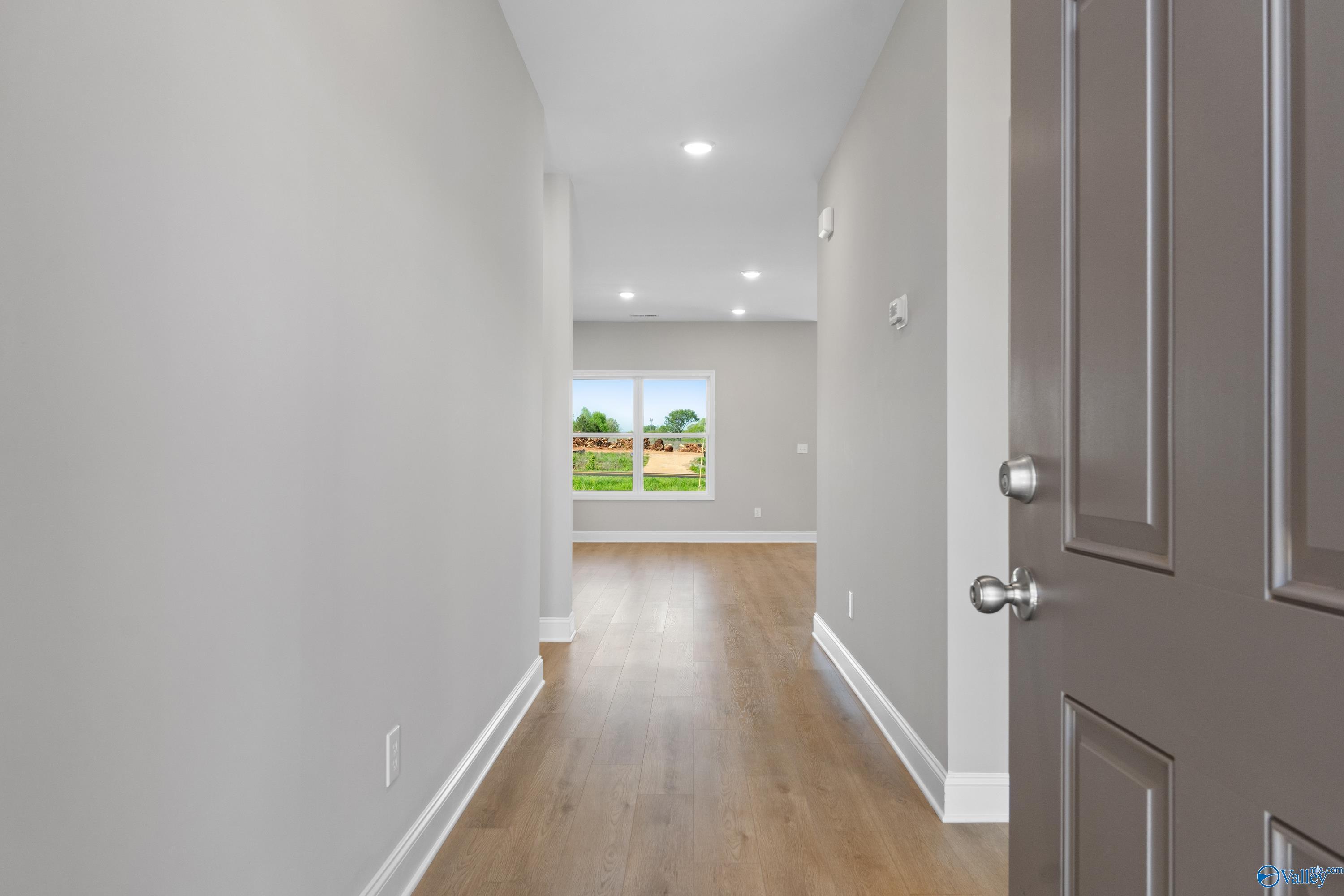 Bright hallway with light oak floors, gray walls, and window view in The Asheville C 3-bedroom home, Athens, Alabama