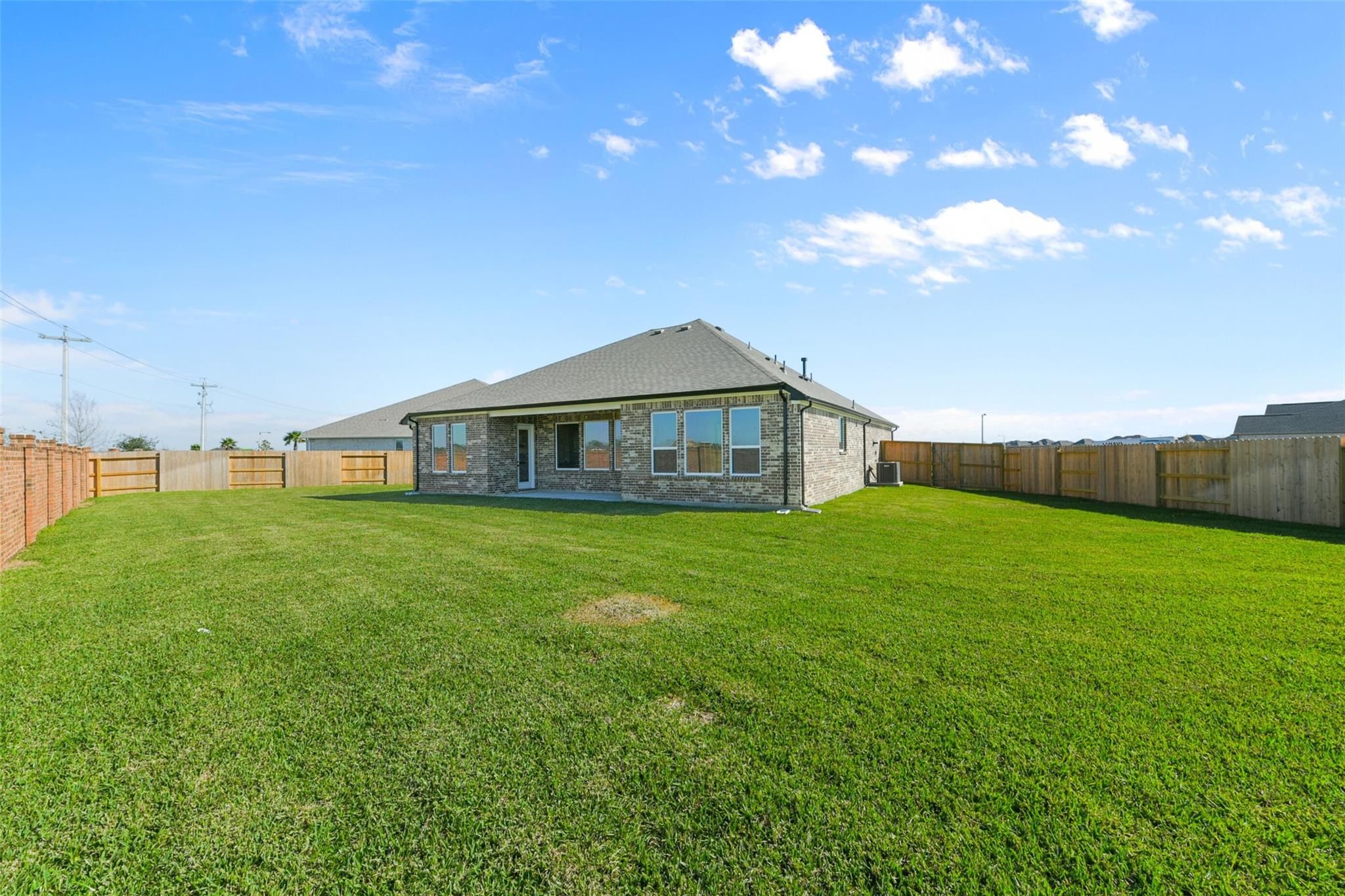 Single-story stone Edward C home by Davidson Homes in Lago Mar, Texas City: covered patio, large windows, fenced lush green yard