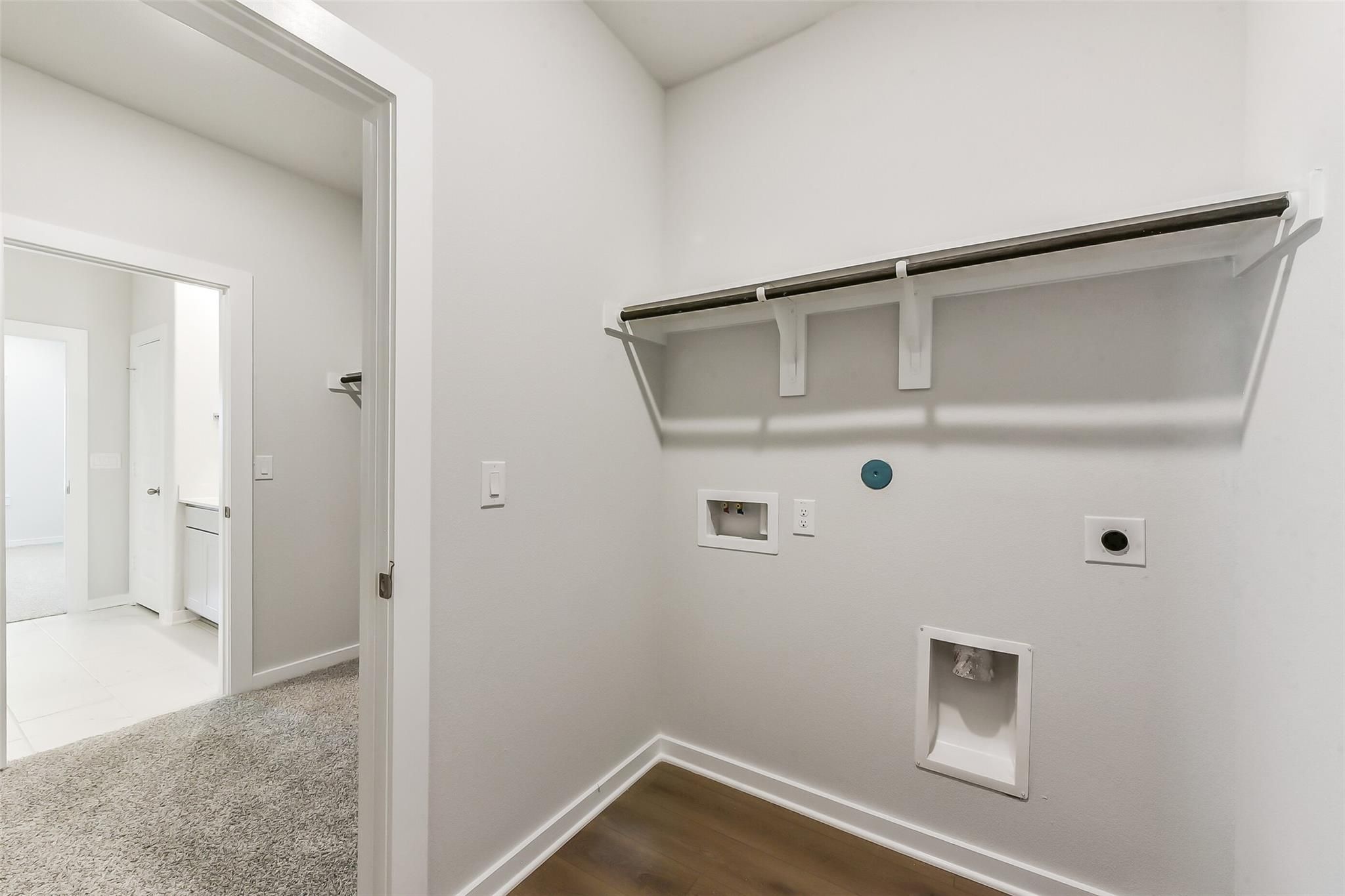 Bright laundry room with utility sink, washer/dryer hookups, shelving, and adjacent bathroom in Davidson Homes The Brazos E, Magnolia, Texas