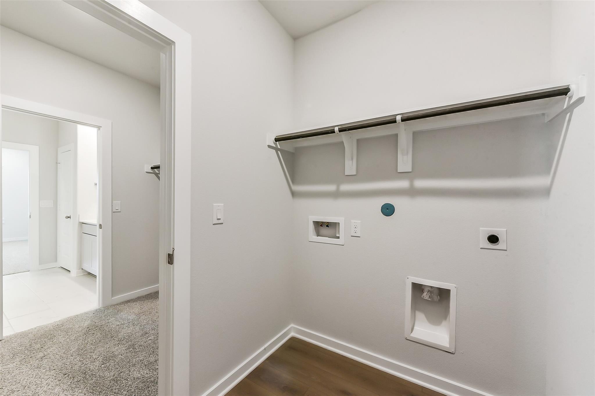 Bright laundry room with utility sink, washer/dryer hookups, shelving, and adjacent bathroom in Davidson Homes The Brazos E, Magnolia, Texas