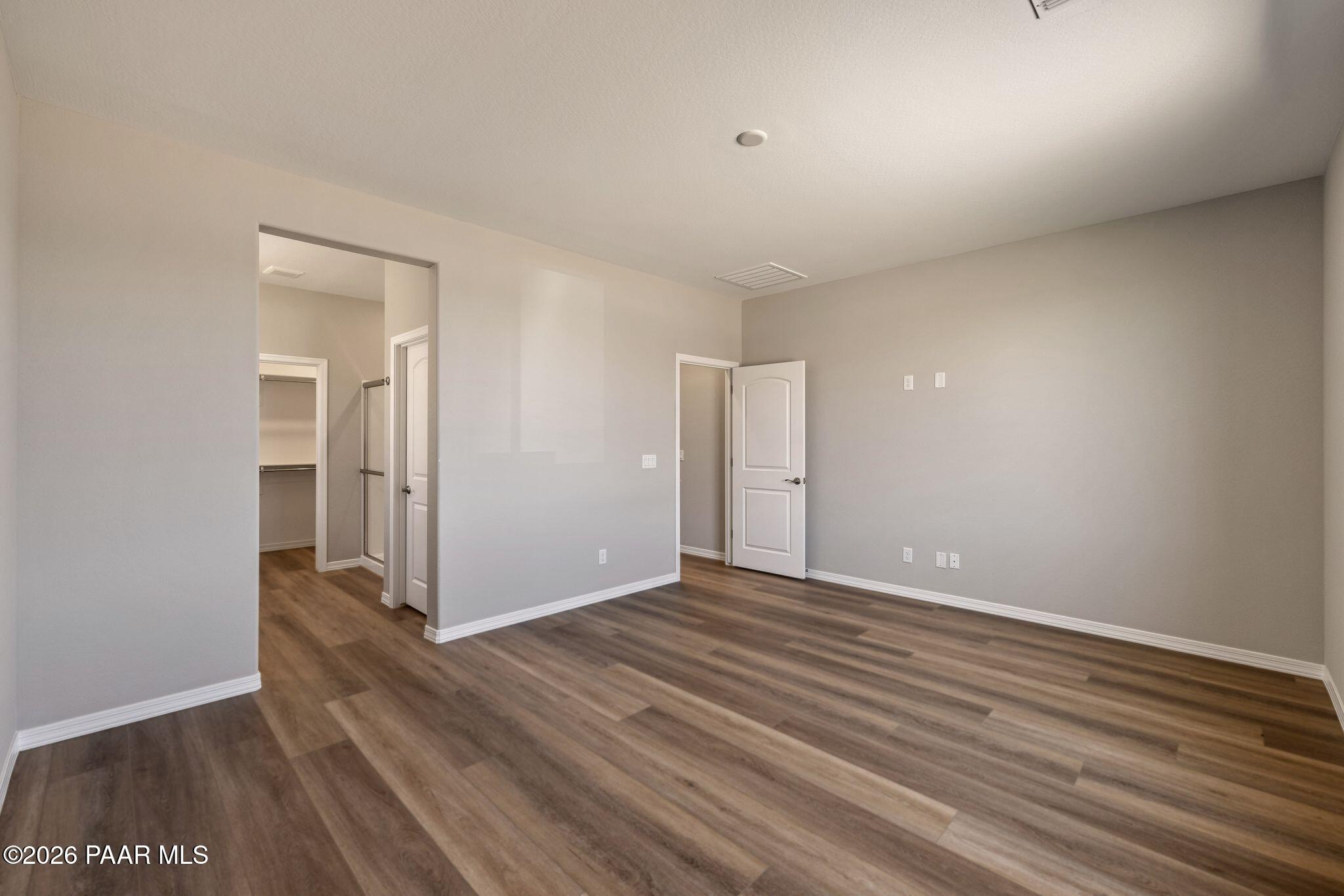 Modern laundry room with neutral beige walls, laminate wood flooring, stacked washer-dryer, and storage shelves in Davidson Homes The Frontier A, Prescott Valley