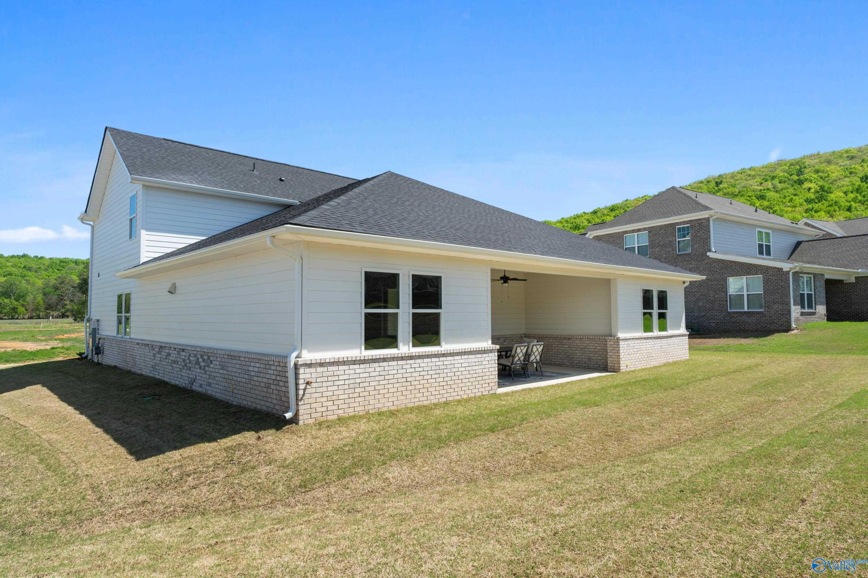 Exterior view of two-story Evermore Homes The Haven featuring covered patio with ceiling fan, brick accents, and lush green lawn in The Meadows at Hampton Cove, Owens Cross Roads, Alabama